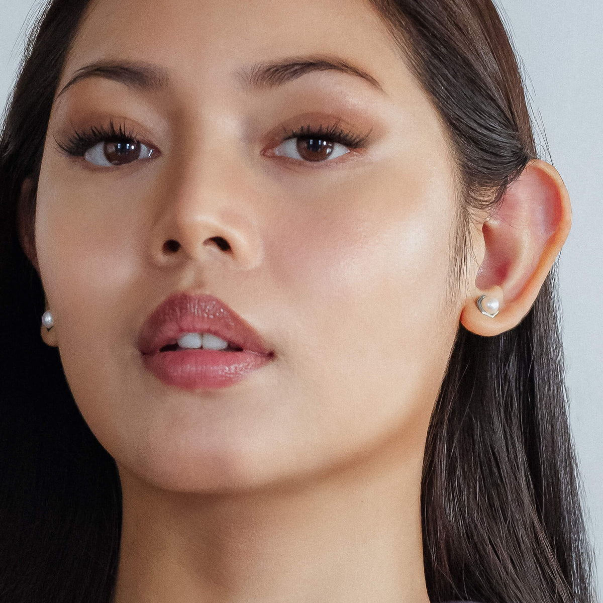 Close-up of a woman's face with earrings on a neutral background