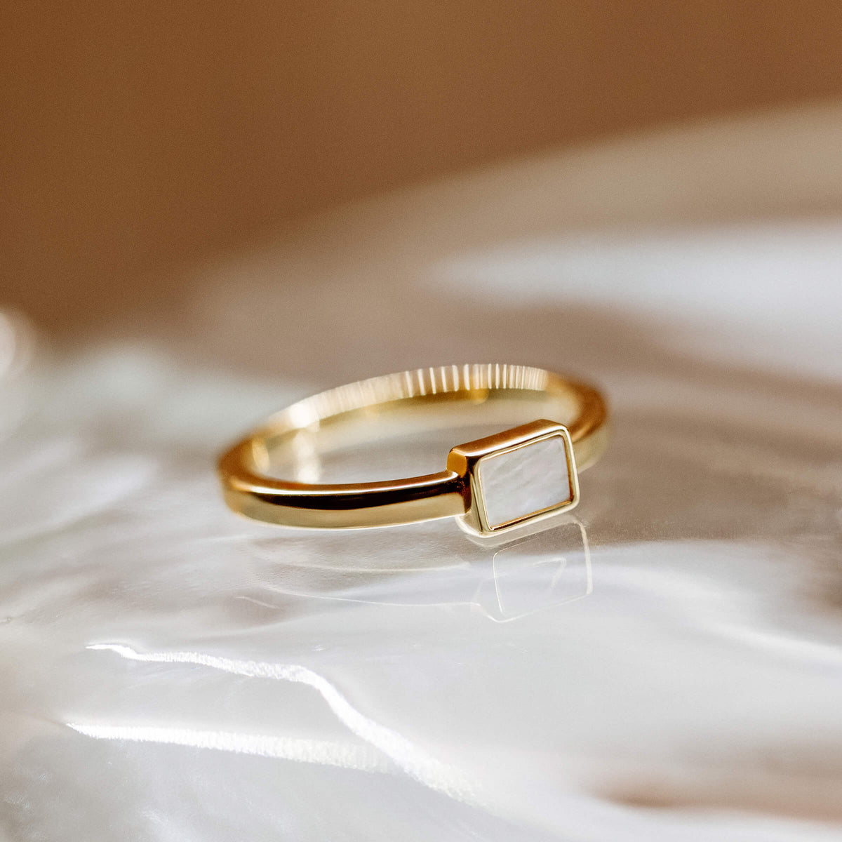 Gold ring with a square mother of pearl on a white surface