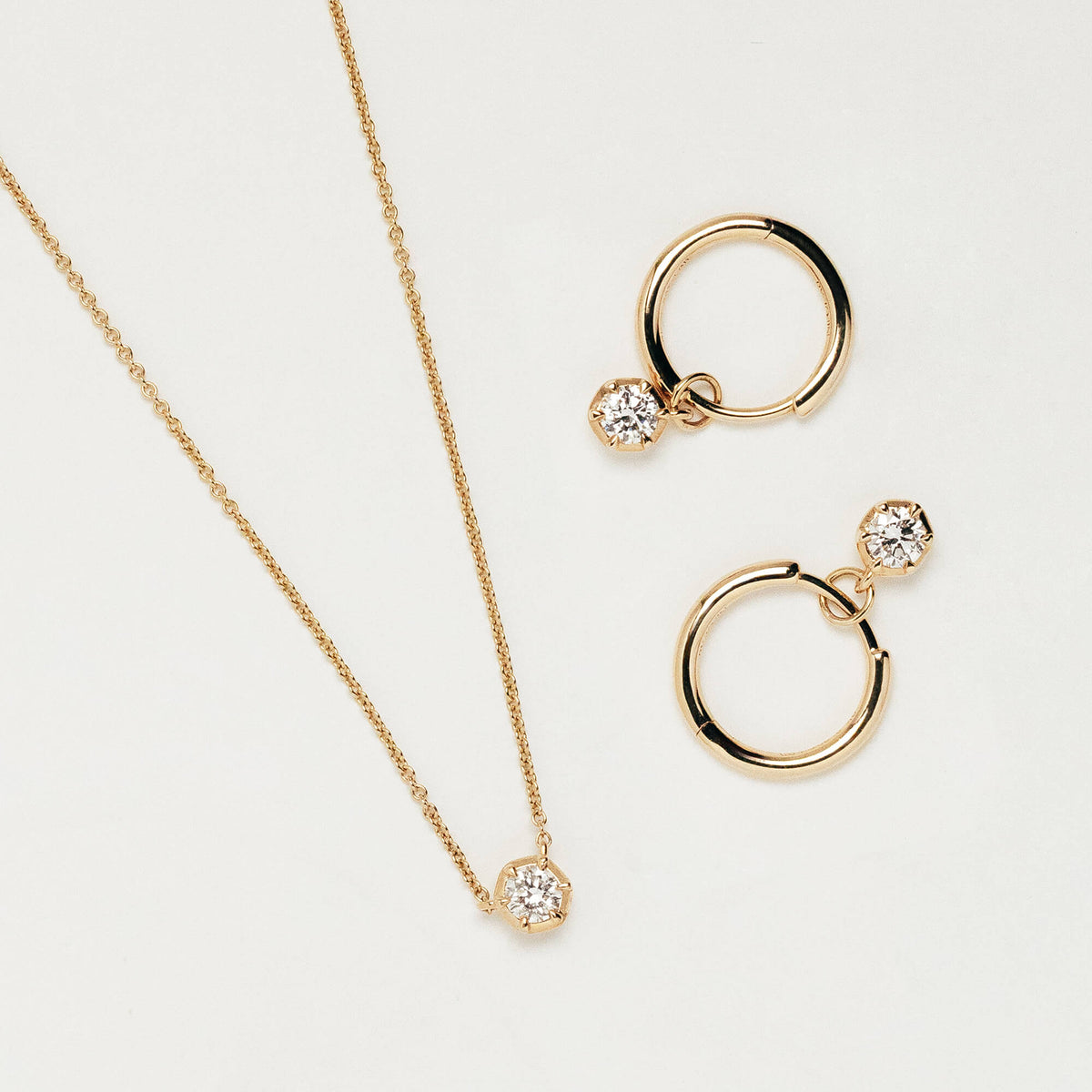 A gold jewellery set featuring a delicate chain necklace with a small round lab diamond pendant, alongside two matching gold hoop earrings, each adorned with a lab diamond, displayed on a clean off-white background. Designed in New Zealand