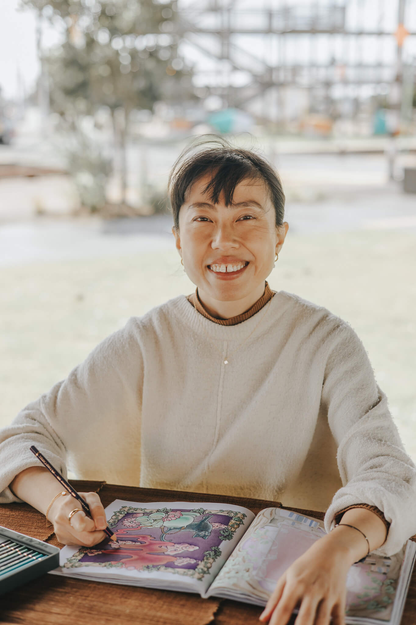 Person sitting at a table with a colorful book open in front of them, smiling outdoors.