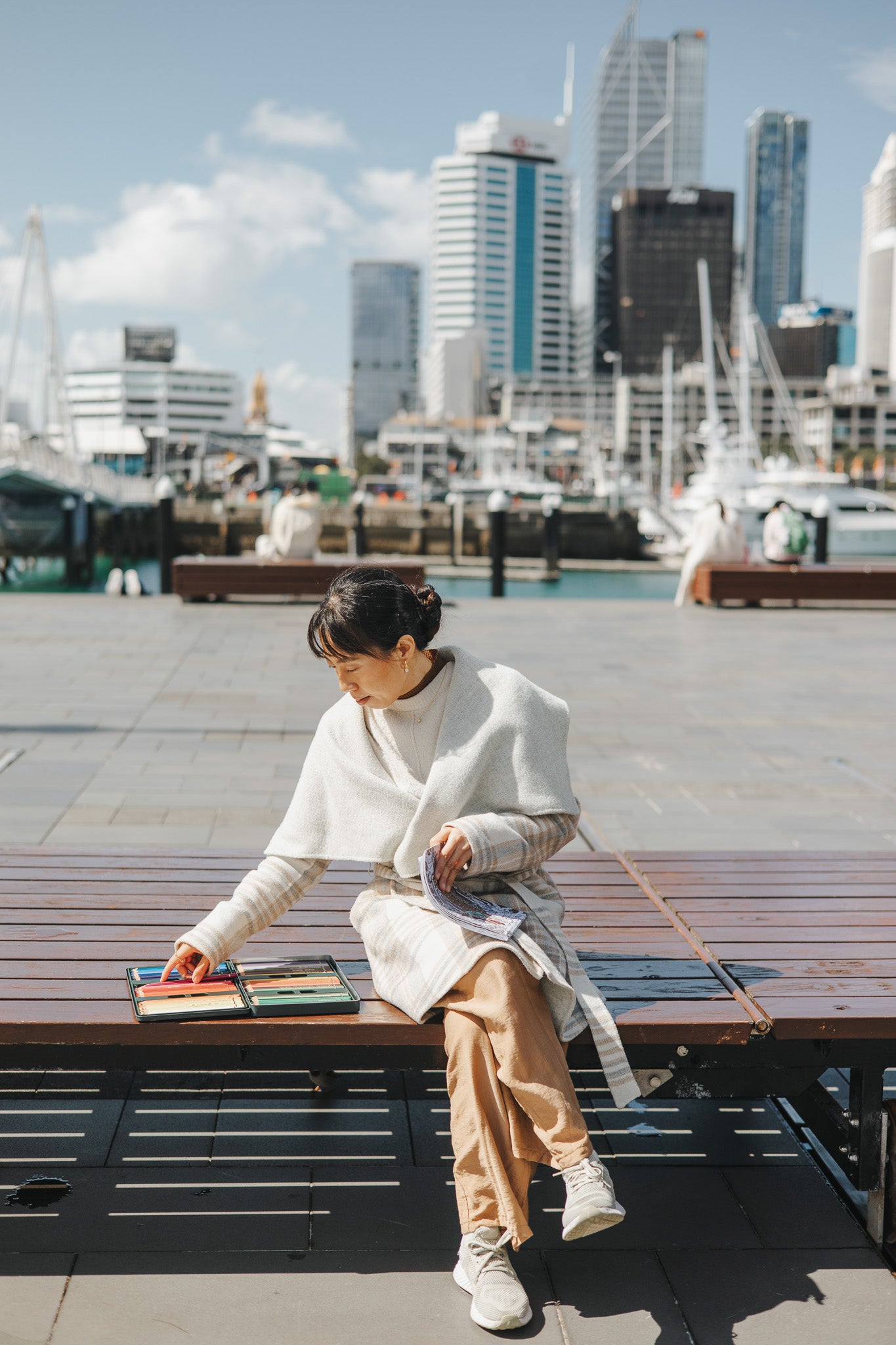 Person sitting on a bench by a waterfront with city skyline in the background