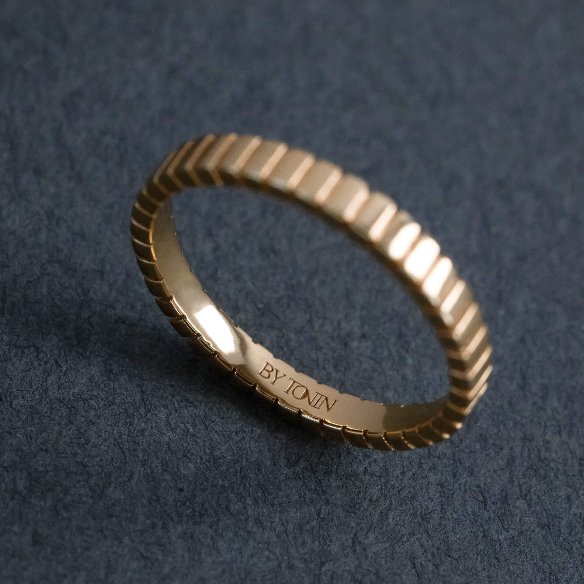 Gold ring with textured ridged band on a dark gray background