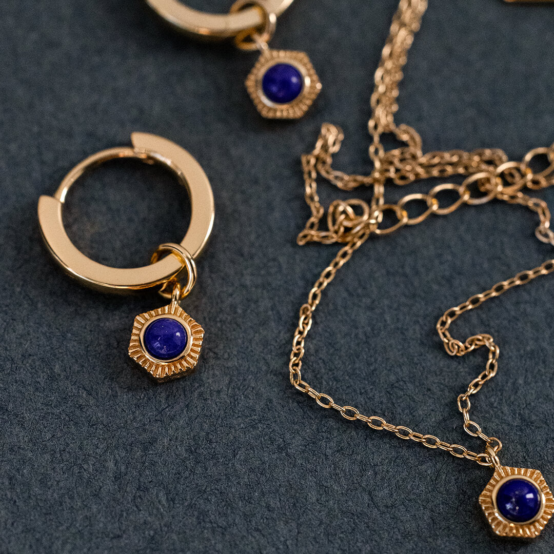 Gold hoop earrings with blue gemstones on a dark surface