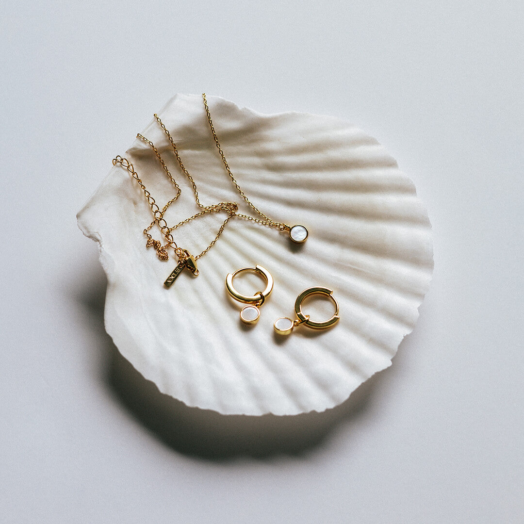 Gold jewelry including necklaces and rings on a white shell against a light gray background