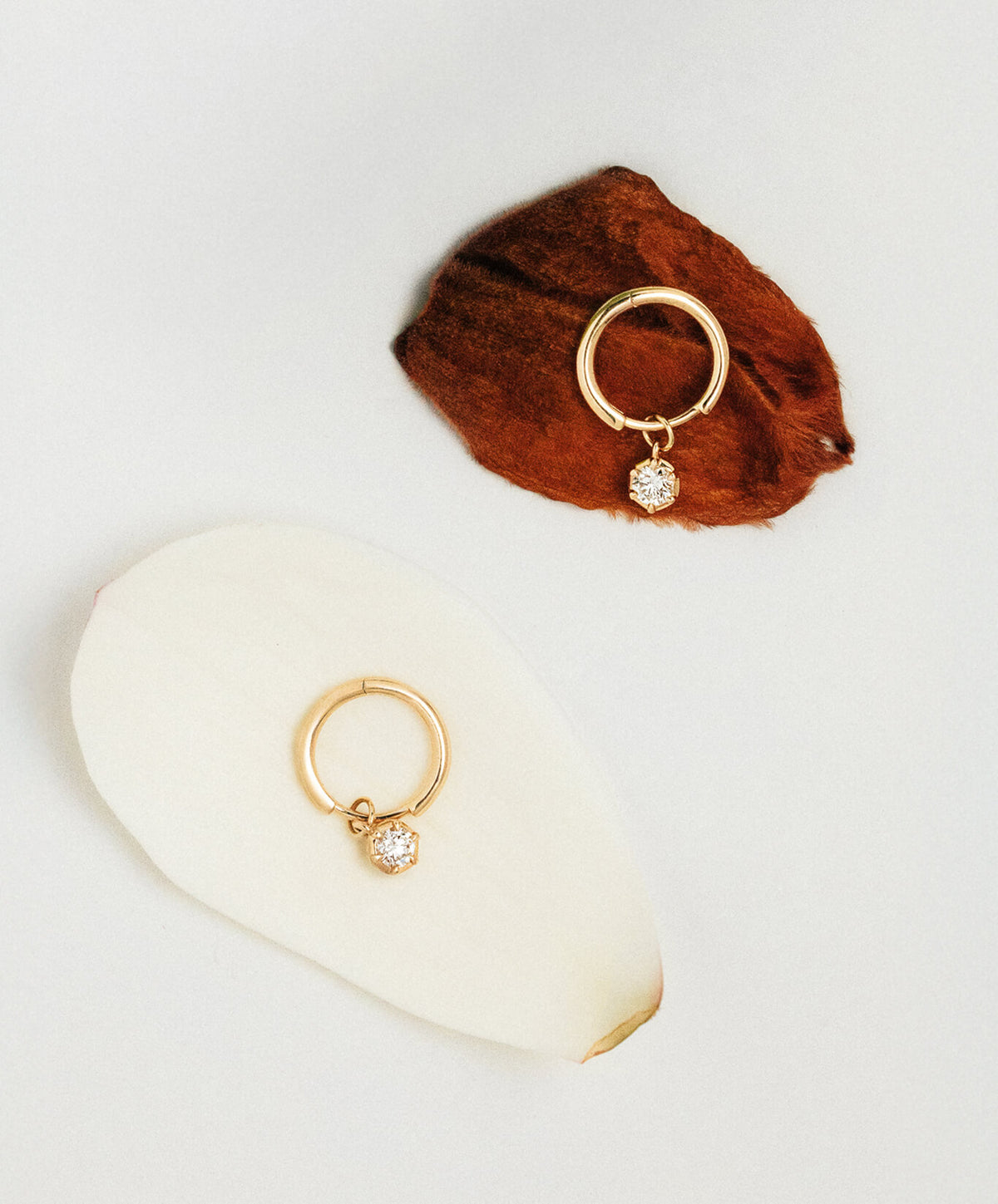Two gold hoop earrings with small clear diamond drops, displayed on a white surface with a brown textured prop.
