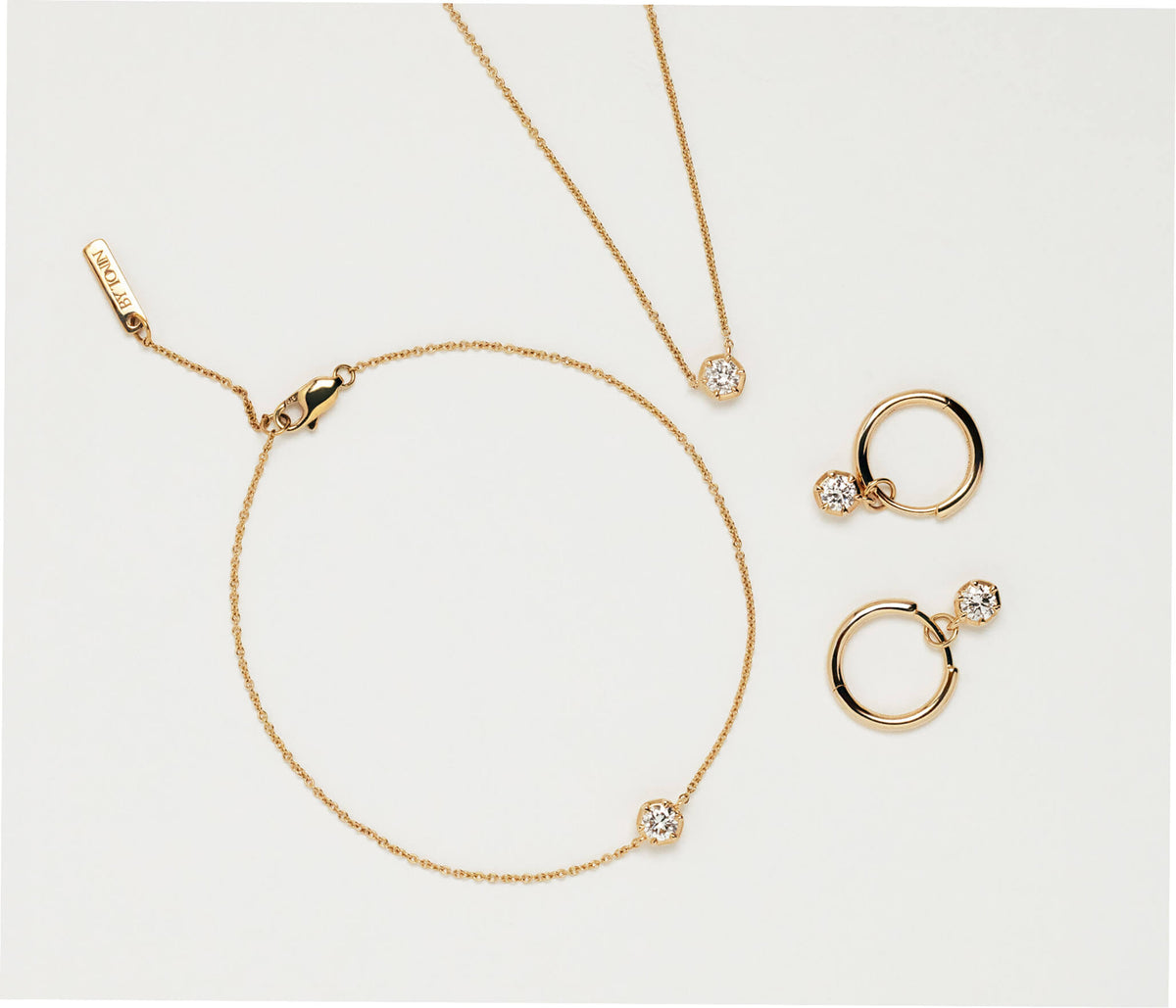 A gold jewellery set in New Zealand featuring a delicate chain necklace, matching bracelet, and hoop earrings, each adorned with a lab diamond displayed on a clean white background.