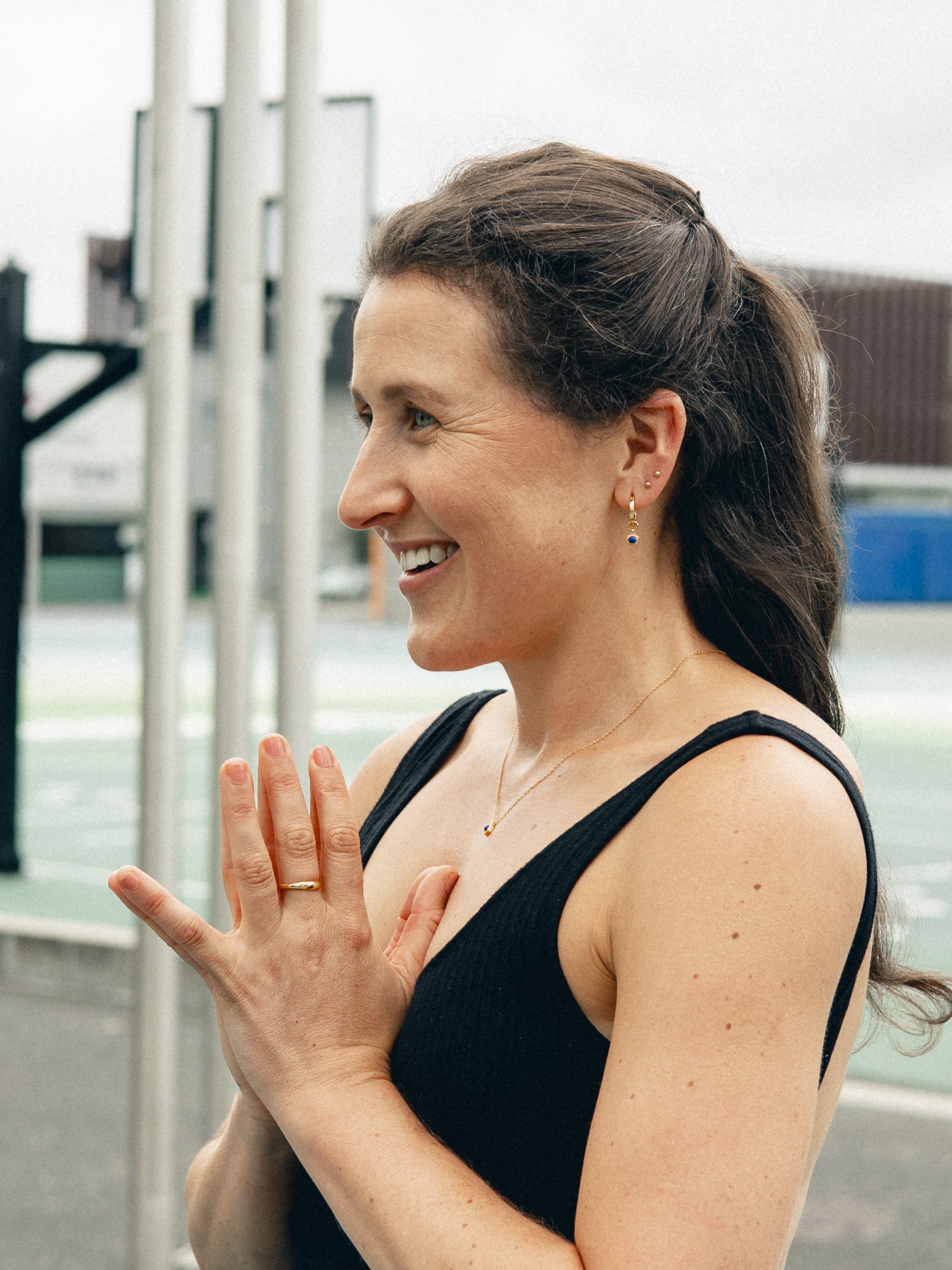 Woman in a black tank top with hands clasped together outdoors