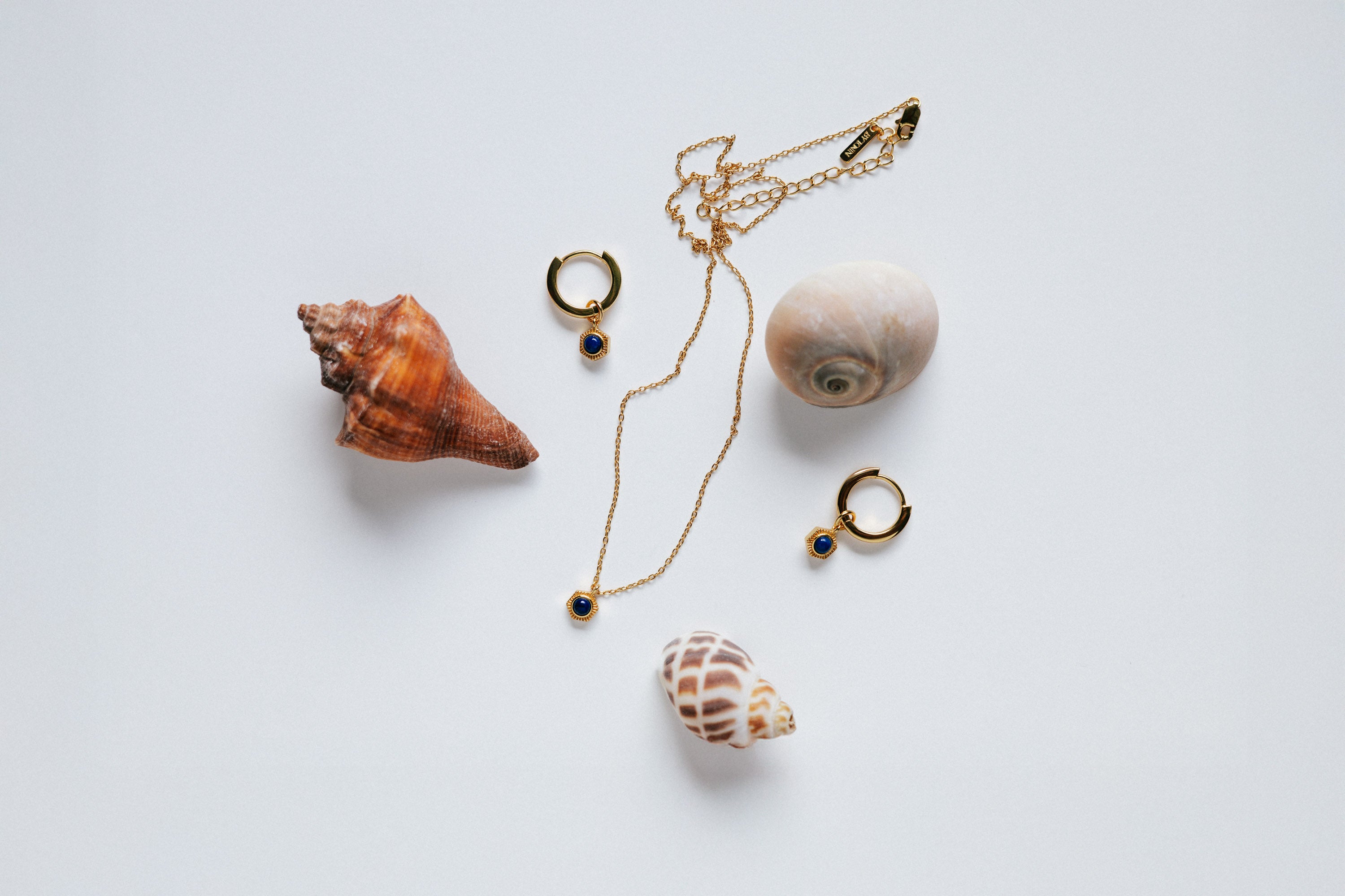 Set - Round Lapis Lazuli pendant necklace and huggie hoop earrings set, styled with mixed natural seashells on a white background