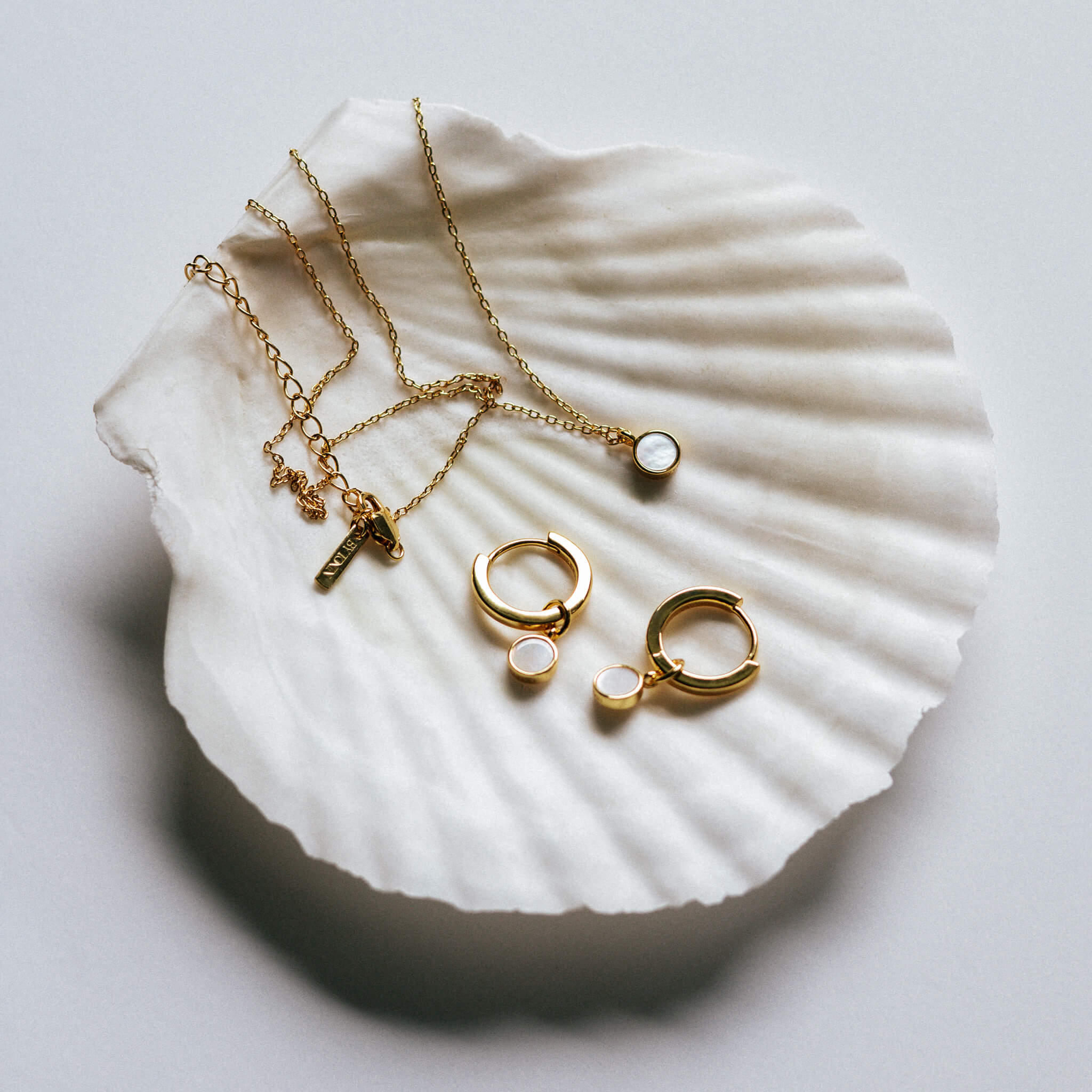 Set - Round Mother of Pearl pendant necklace and huggie hoop earrings set, displayed on a large white Scallop seashell.
