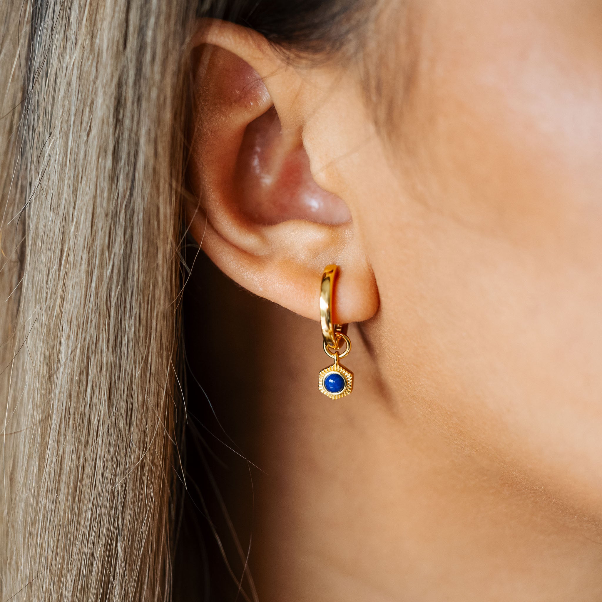 Adorn your ear with BY TONIN's captivating Bel e Viv gold hoop earring, beautifully showcasing a hexagonal deep blue lapis lazuli charm in a striking close-up.