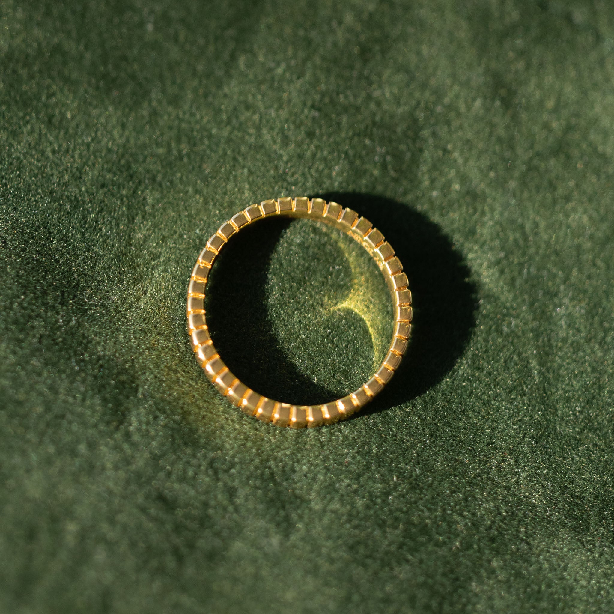 Experience the exquisite texture of BY TONIN's Bel e Viv gold ridged ring, elegantly displayed on a luxurious green velvet surface, inviting a touch of modern sophistication.