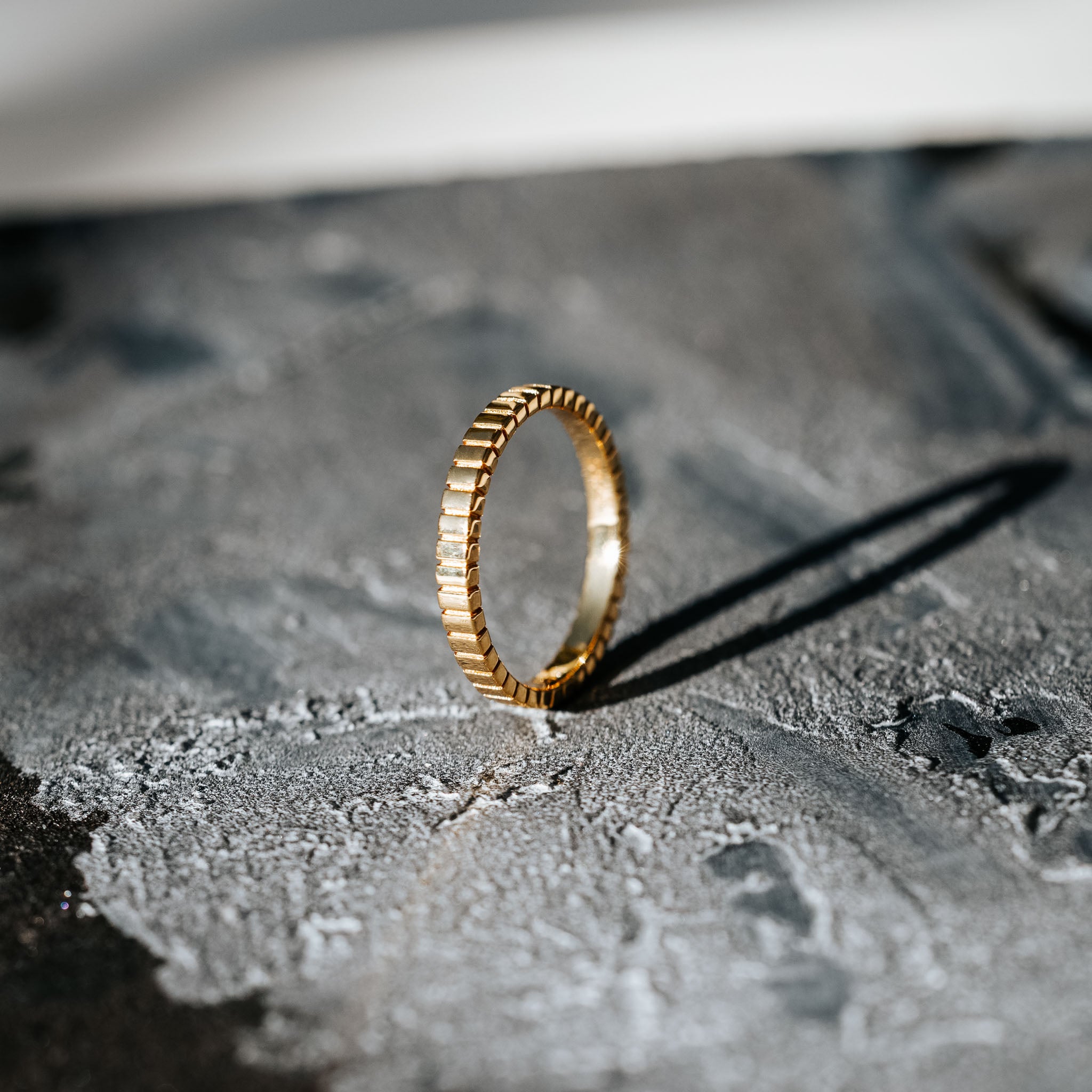 Showcase your unique style with BY TONIN's Bel e Viv gold ridged ring, dramatically presented upright on a captivating textured grey surface, highlighting its distinctive design.
