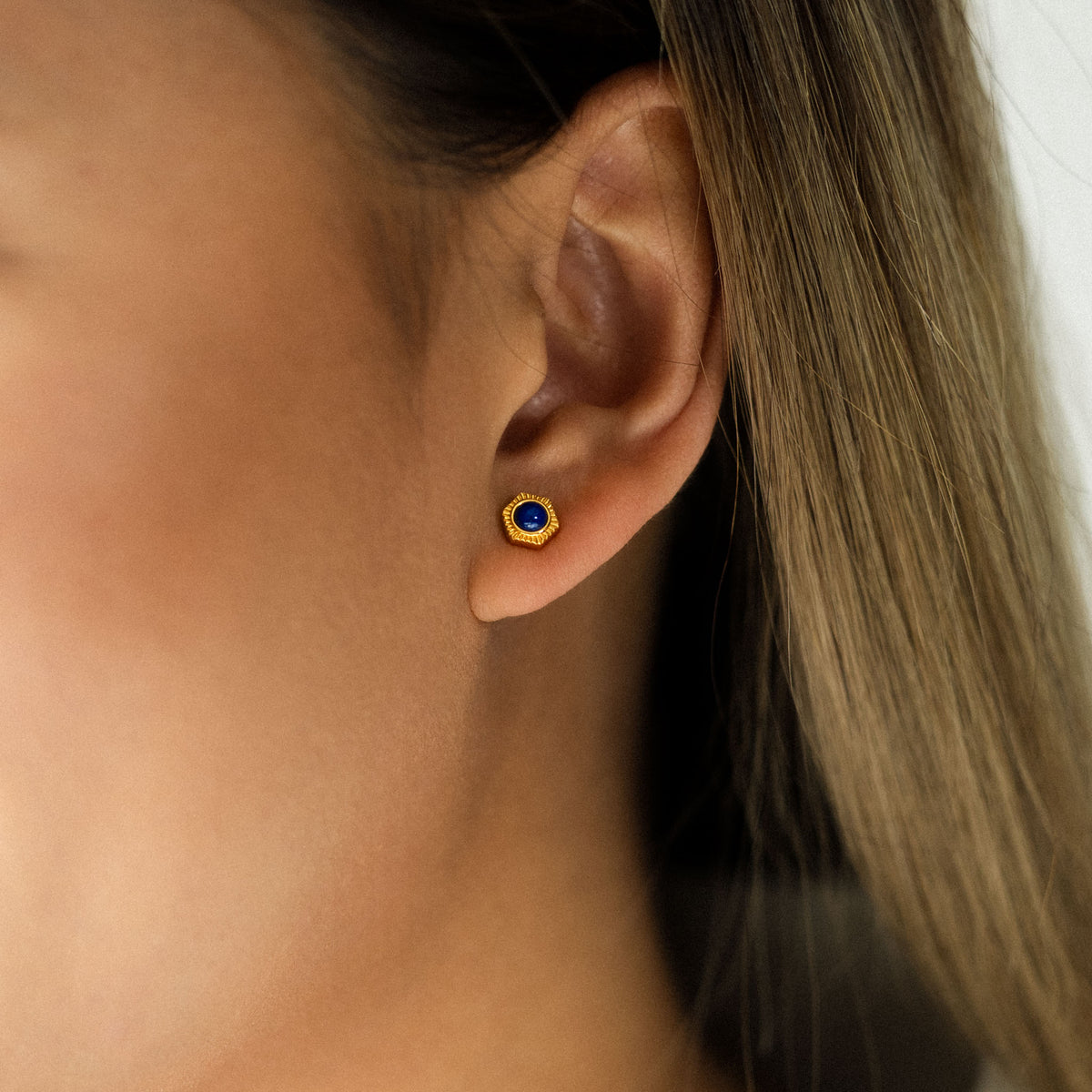 Adorn your ear with BY TONIN's captivating Bel e Viv gold hexagon stud earring, beautifully showcasing a deep blue lapis lazuli gemstone in a striking close-up.