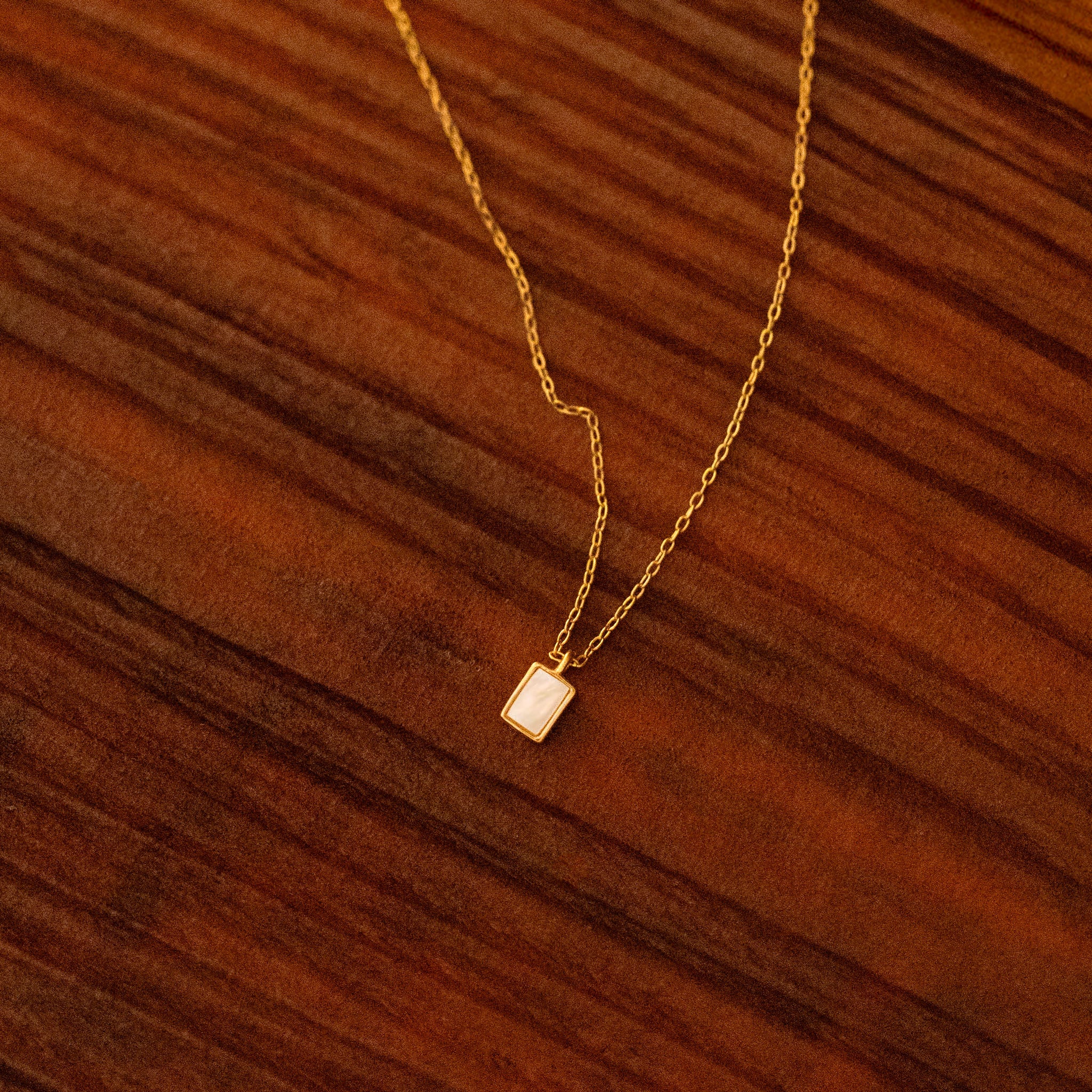 Illuminate your neckline with BY TONIN's Heritage gold necklace, featuring a luminous baguette mother of pearl pendant, gracefully presented on a rich wooden surface.