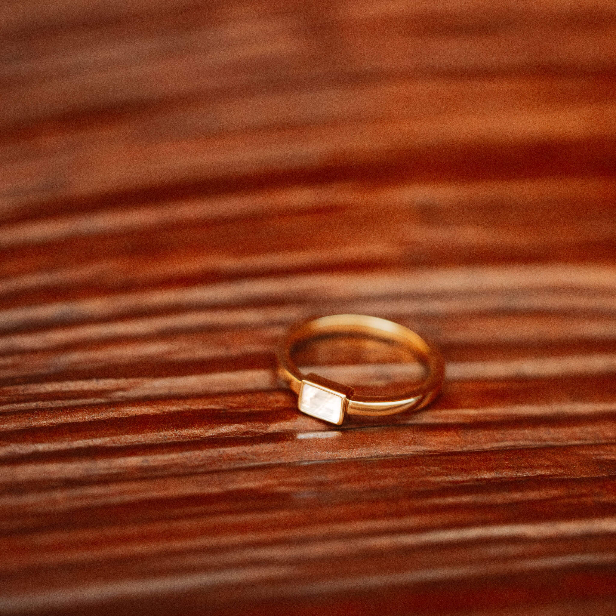 Discover the captivating glow of BY TONIN's Heritage gold ring, featuring a luminous rectangular mother of pearl centerpiece, artfully displayed on a warm wooden surface.