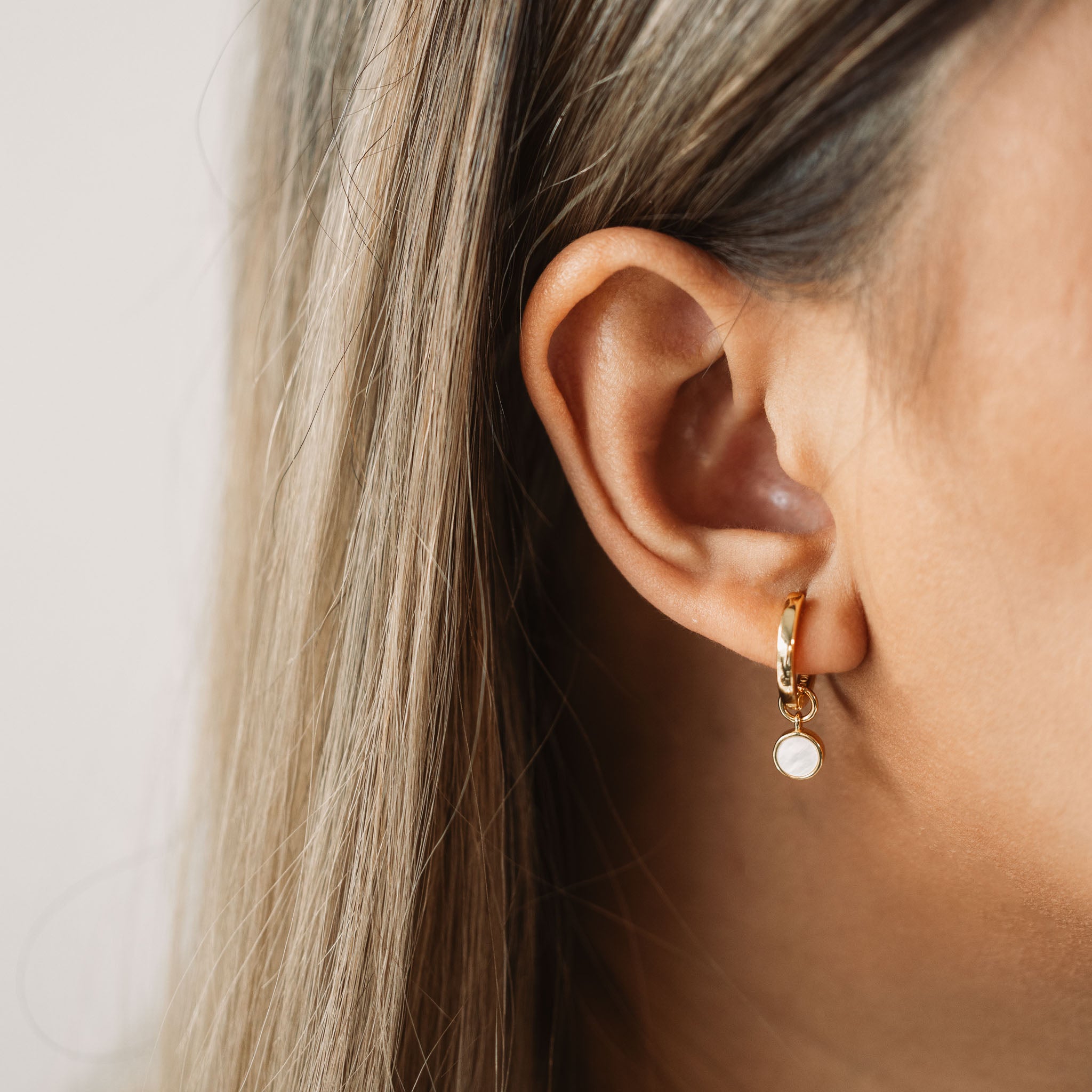 Adorn your ear with BY TONIN's Heritage gold mini hoop earring, gracefully showcasing a luminous round mother of pearl charm in a beautiful close-up, epitomizing subtle elegance.