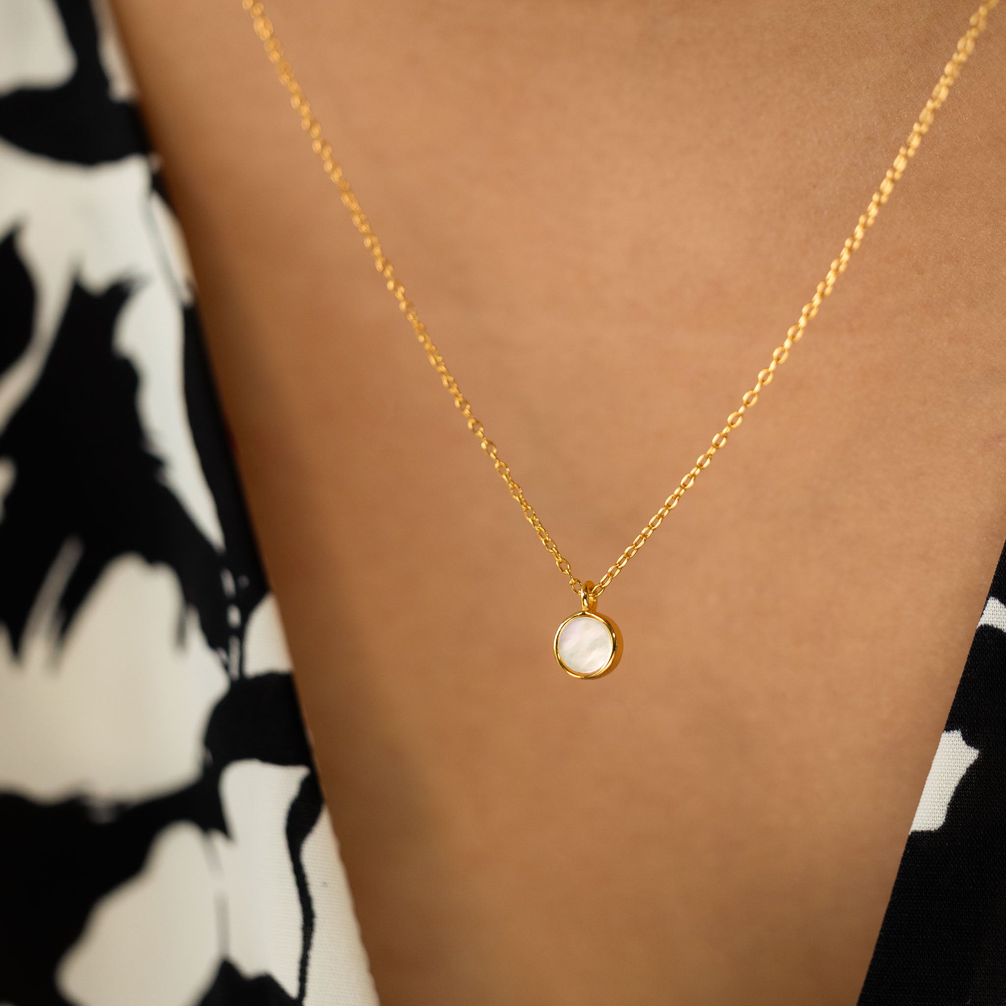 Highlight your neckline with BY TONIN's Heritage gold necklace, beautifully worn to showcase its luminous round mother of pearl pendant against a stylish patterned dress.