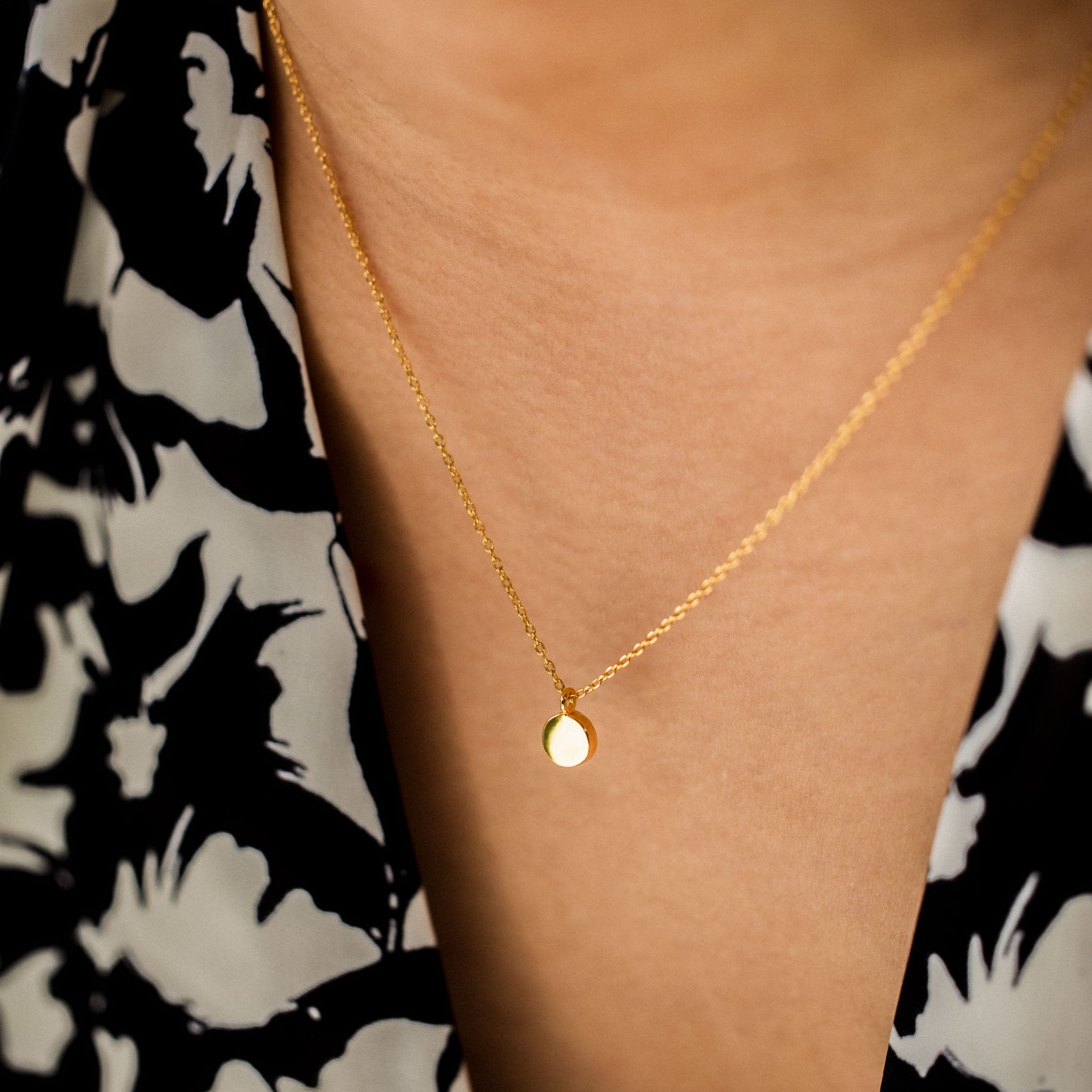 Adorn your décolletage with BY TONIN's Heritage gold necklace, gracefully showcasing a round gold pendant as worn against a striking floral pattern.