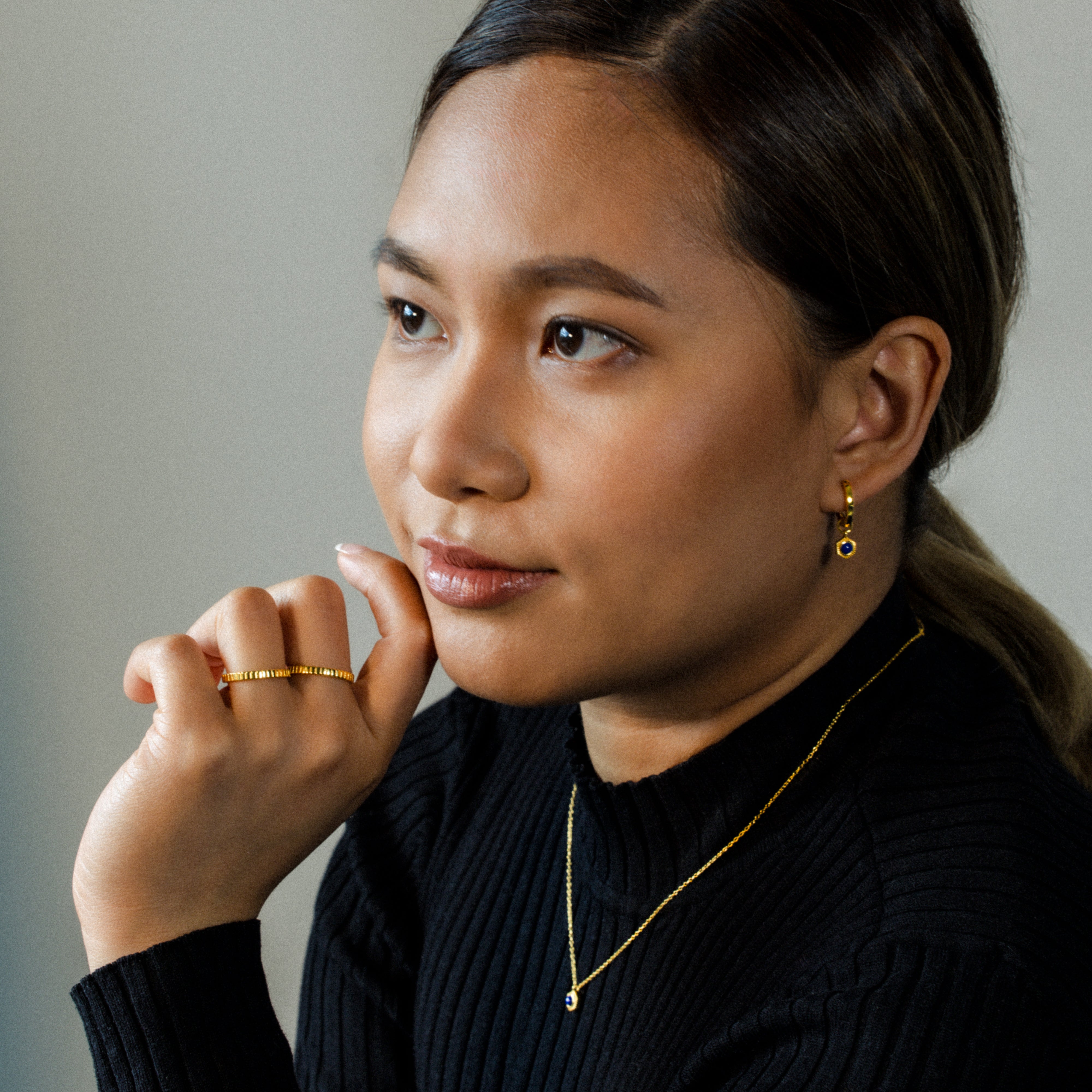 Camille Malazo Dela Cruz, with her radiant warm complexion, elegantly models BY TONIN's exquisite gold lapis lazuli hexagon earrings, stacking ridged rings, and a delicate gold necklace.
