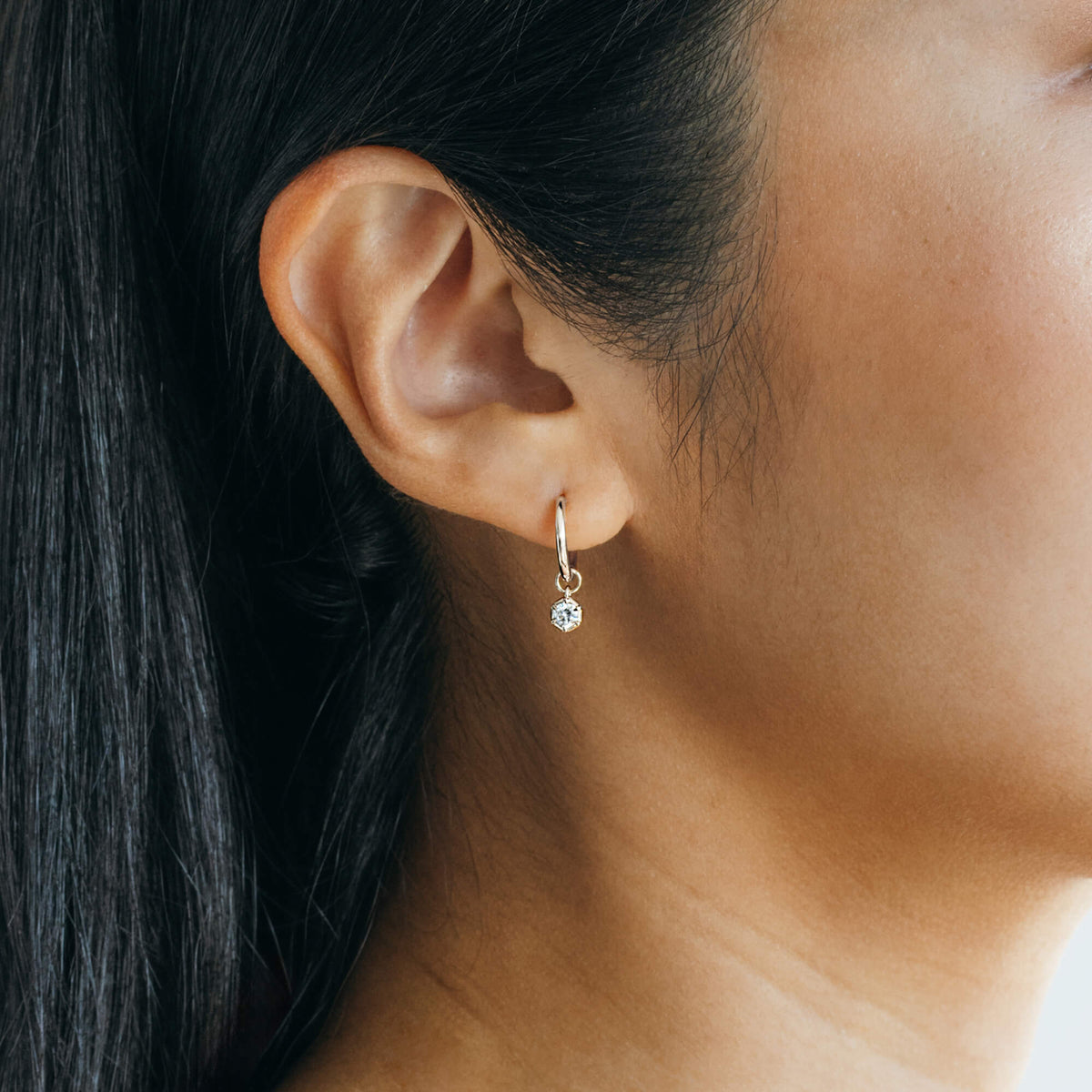 Detailed close-up of a 925 sterling silver small hoop earring featuring a single bezel-set lab-grown diamond drop charm, demonstrating scale and clarity against the skin for a considered wardrobe foundation