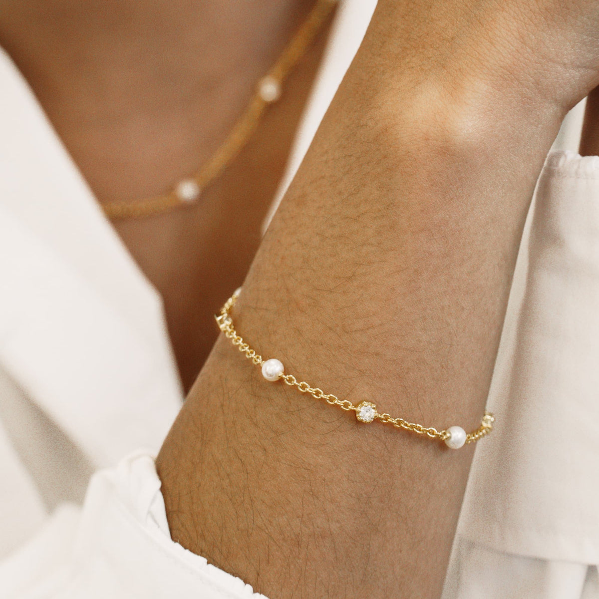 Gold bracelet with topaz and pearls on a person's ankle against a neutral background