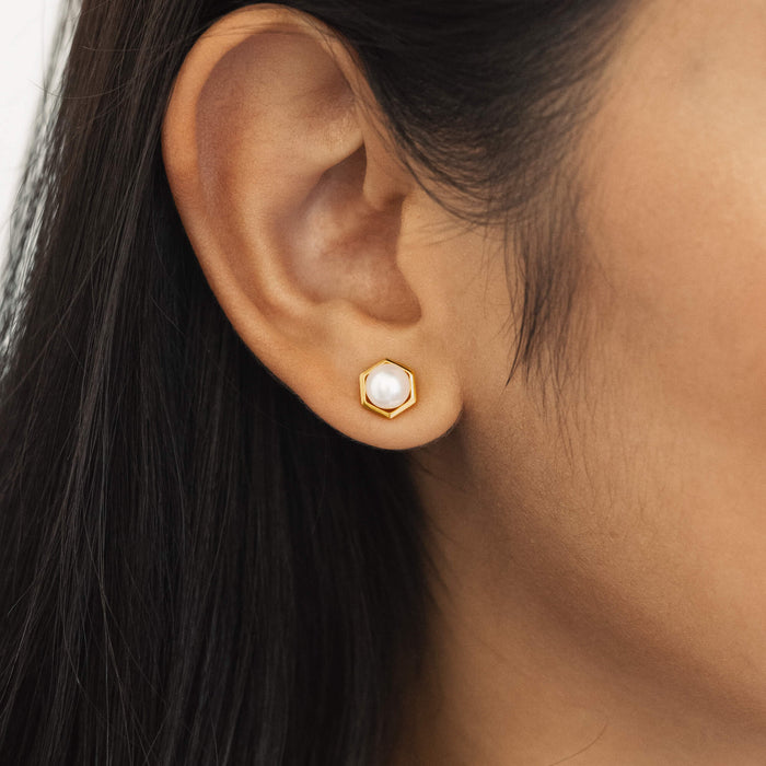 Close-up of an ear wearing a gold earring with a pearl center.