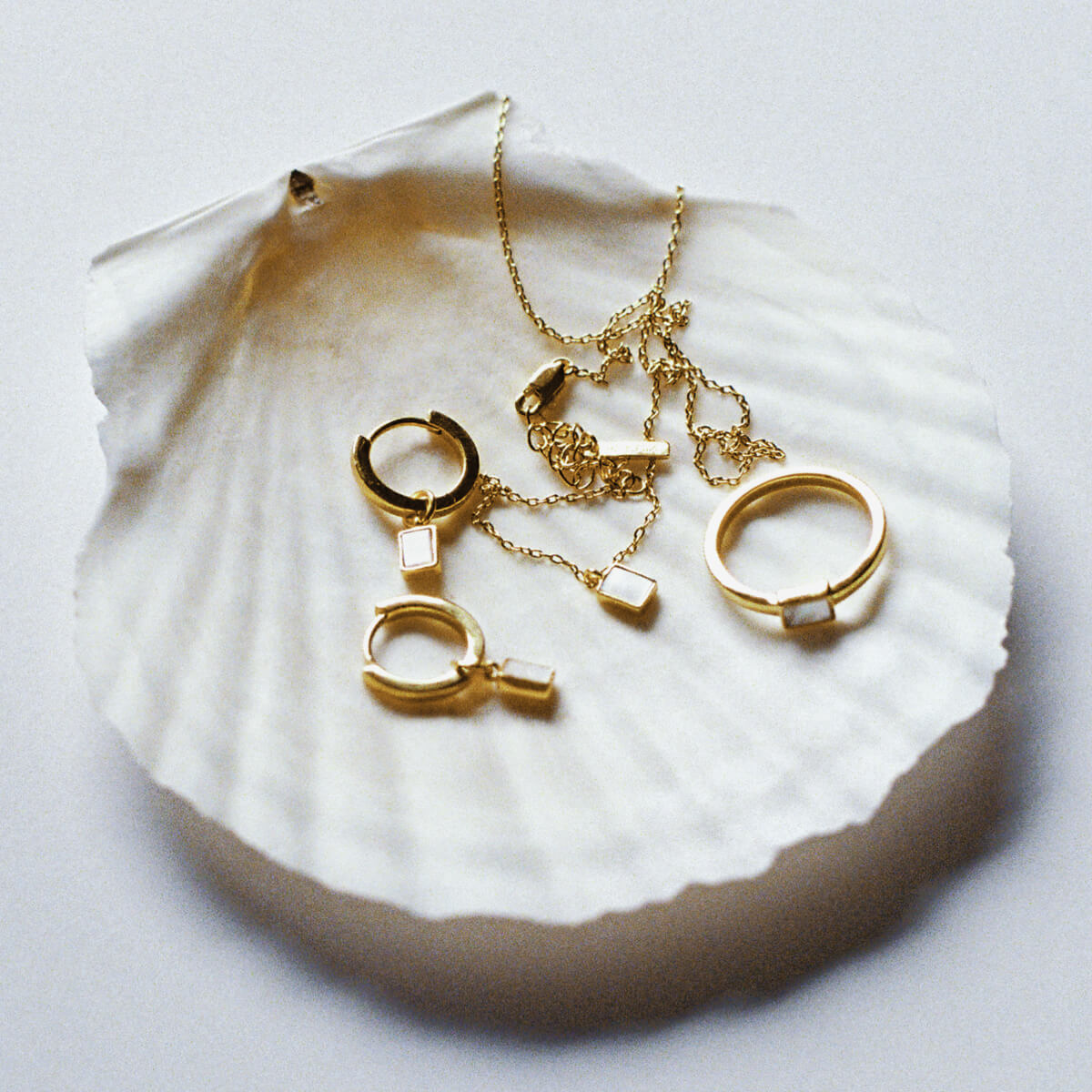 Gold jewellery including earrings, rings and a necklace with Mother of Pearl on a white shell.