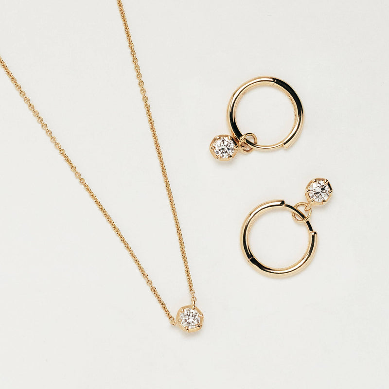 A gold jewellery set featuring a delicate chain necklace with a small round lab diamond pendant, alongside two matching gold hoop earrings, each adorned with a lab diamond, displayed on a clean off-white background. Designed in New Zealand