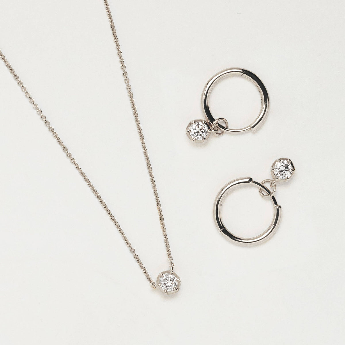 Silver jewellery set featuring a delicate chain necklace with a small round lab diamond pendant, paired with matching hoop earrings, each adorned with a small clear lab diamond drop, displayed on a clean white background.