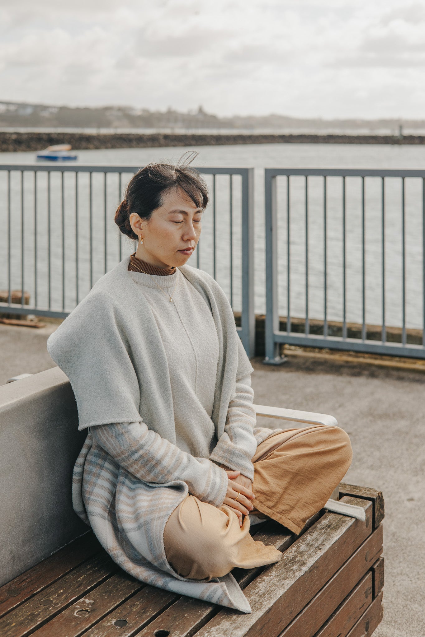 Person sitting on a wooden bench by a railing with a cloudy sky in the background