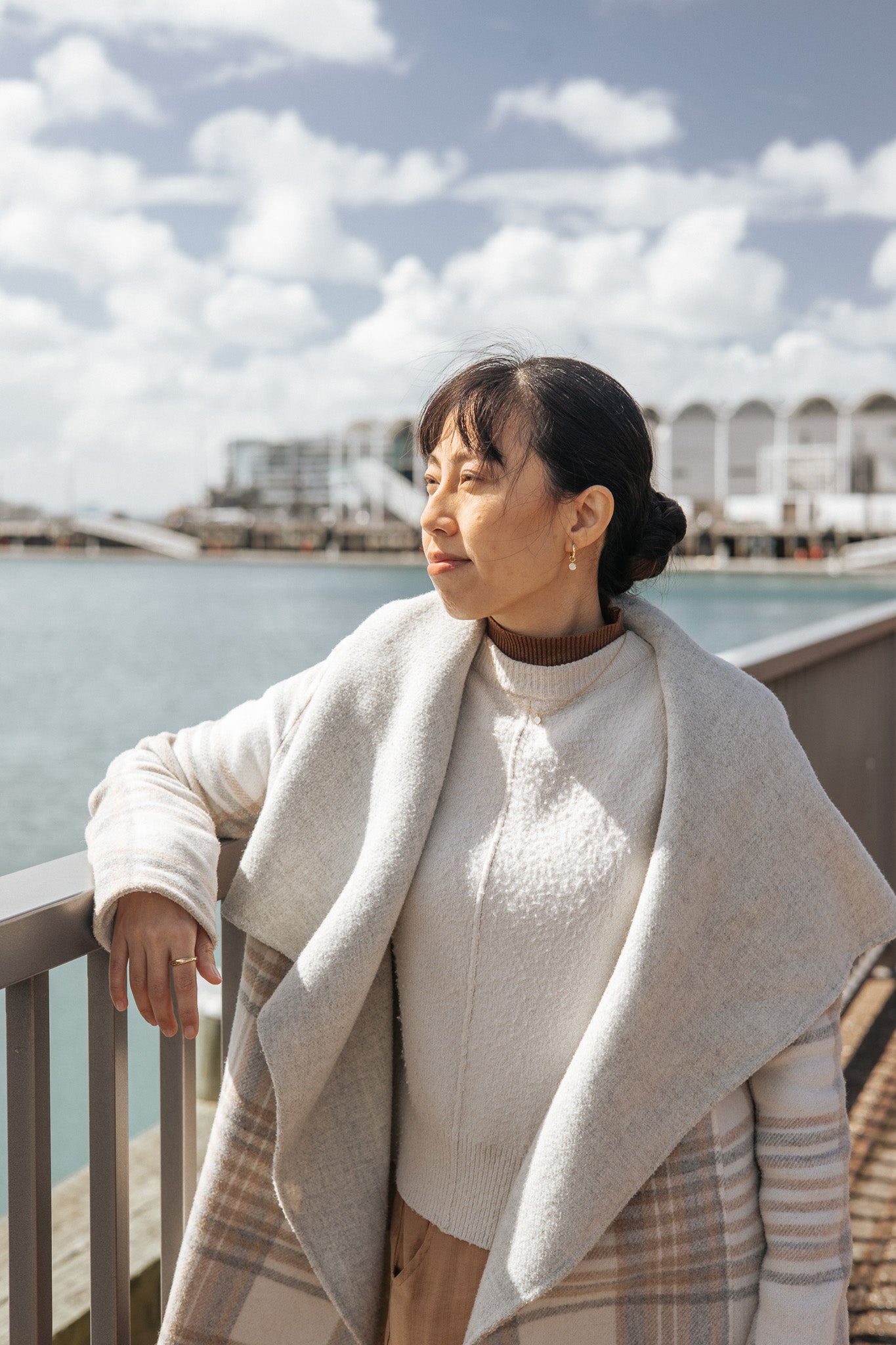 Woman standing by a waterfront with a light-colored coat and sweater at Auckland Viaduct