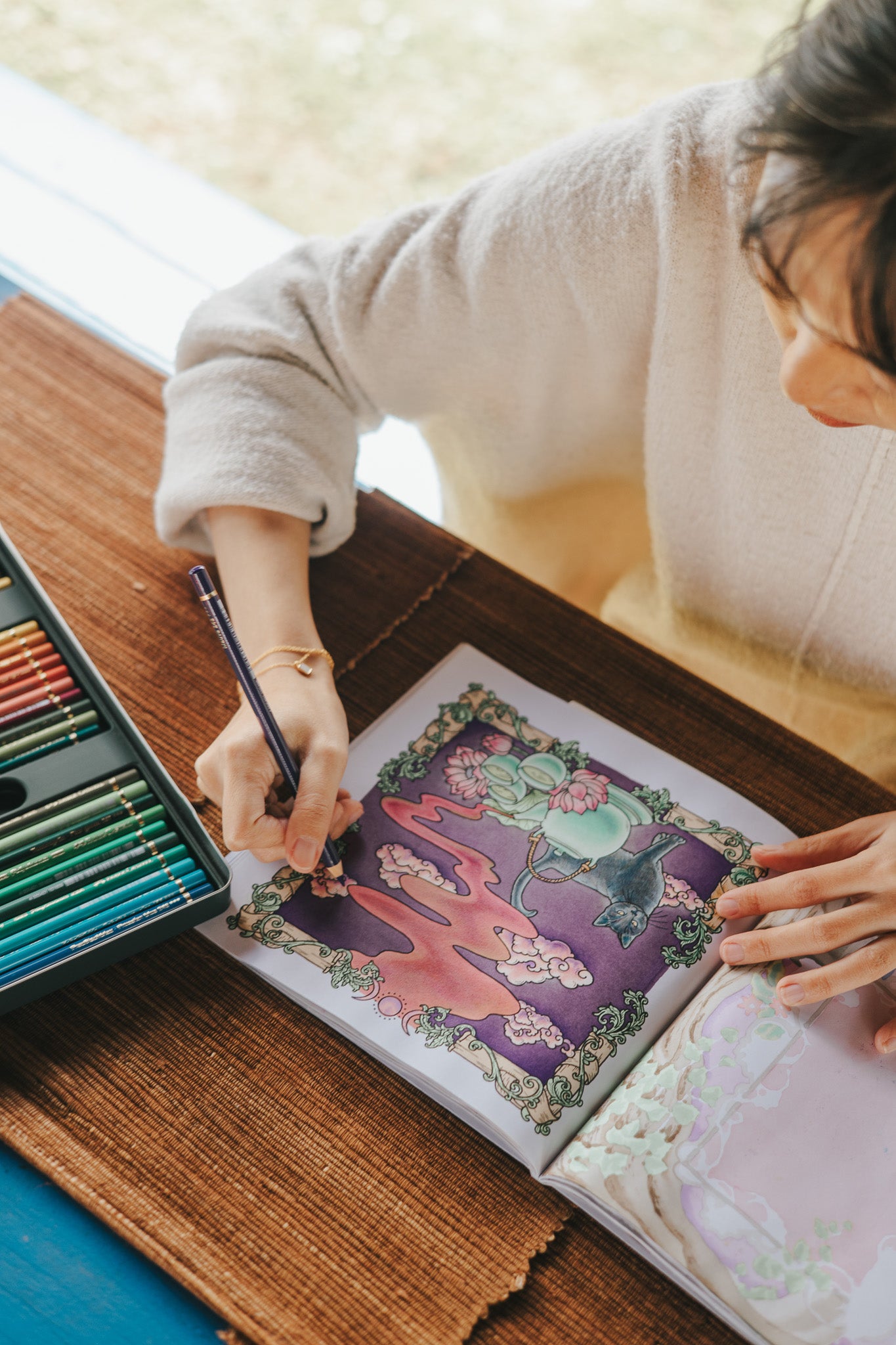 Person coloring a picture of a cat with colored pencils on a wooden table.