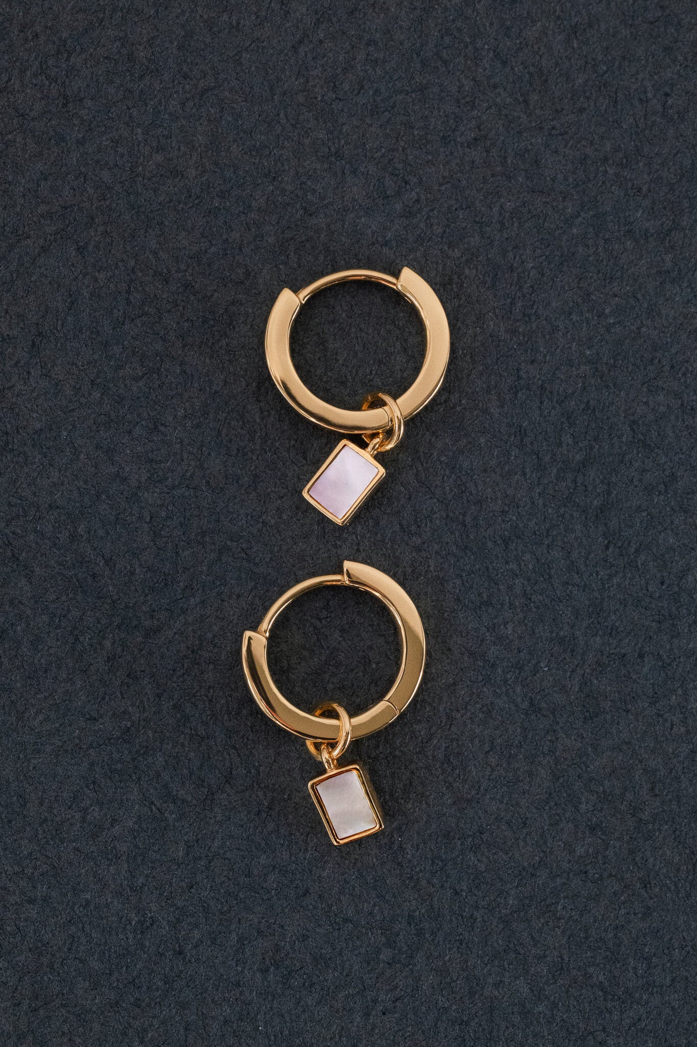 Pair of gold hoop earrings with rectangular baguette mother of pearl charms on a dark background