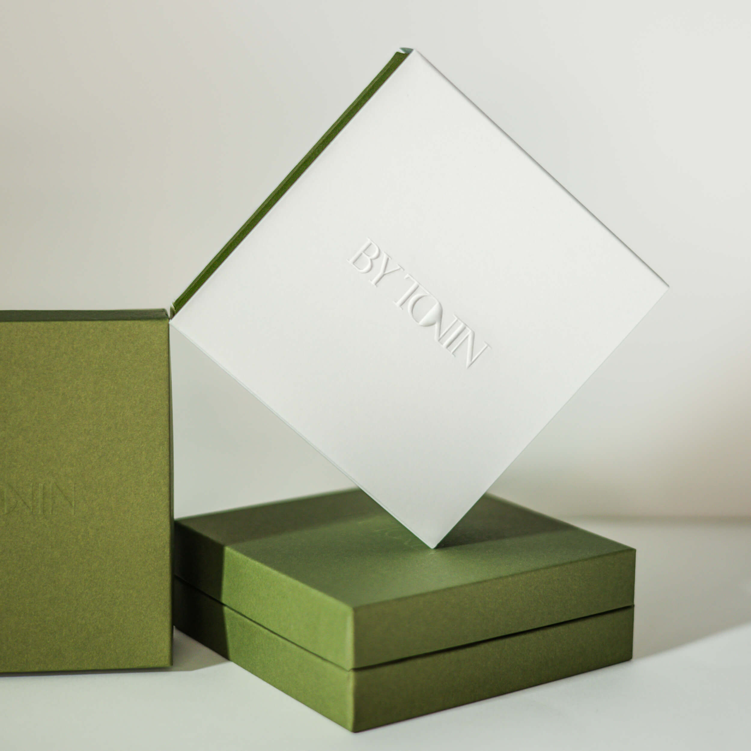 Green and white jewellery luxury box packaging with 'BY TONIN' branding on a light background