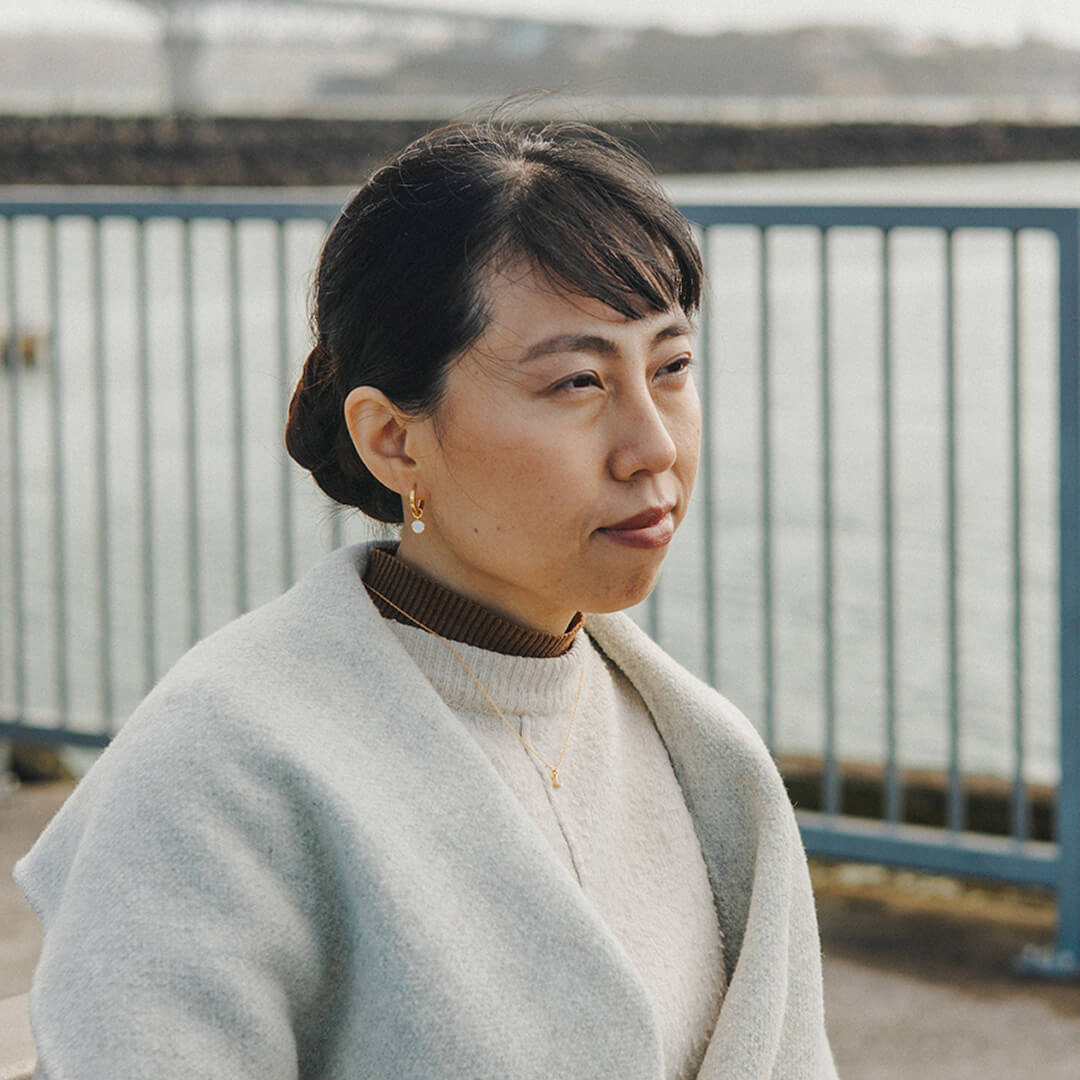 Woman wearing a light gray coat and brown turtleneck against a blurred background