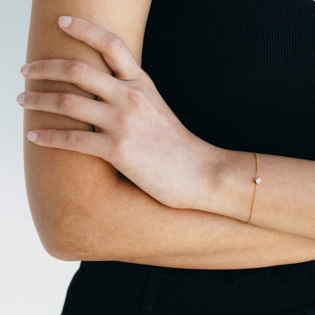 A model with folded arms wearing the dainty 9K gold chain bracelet. The shot highlights how the delicate diamond bracelet sits naturally against the skin, perfect for minimalist jewellery layering.
