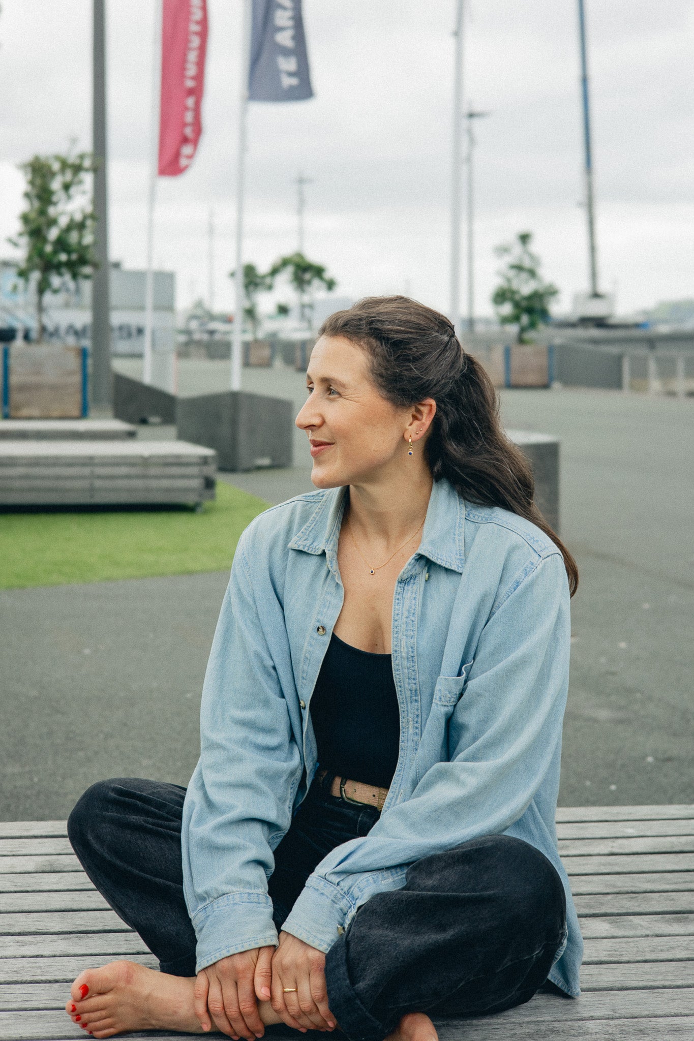 Lifestyle Shot - Model seated outside, wearing gold minimalist necklace and earrings with a denim shirt.