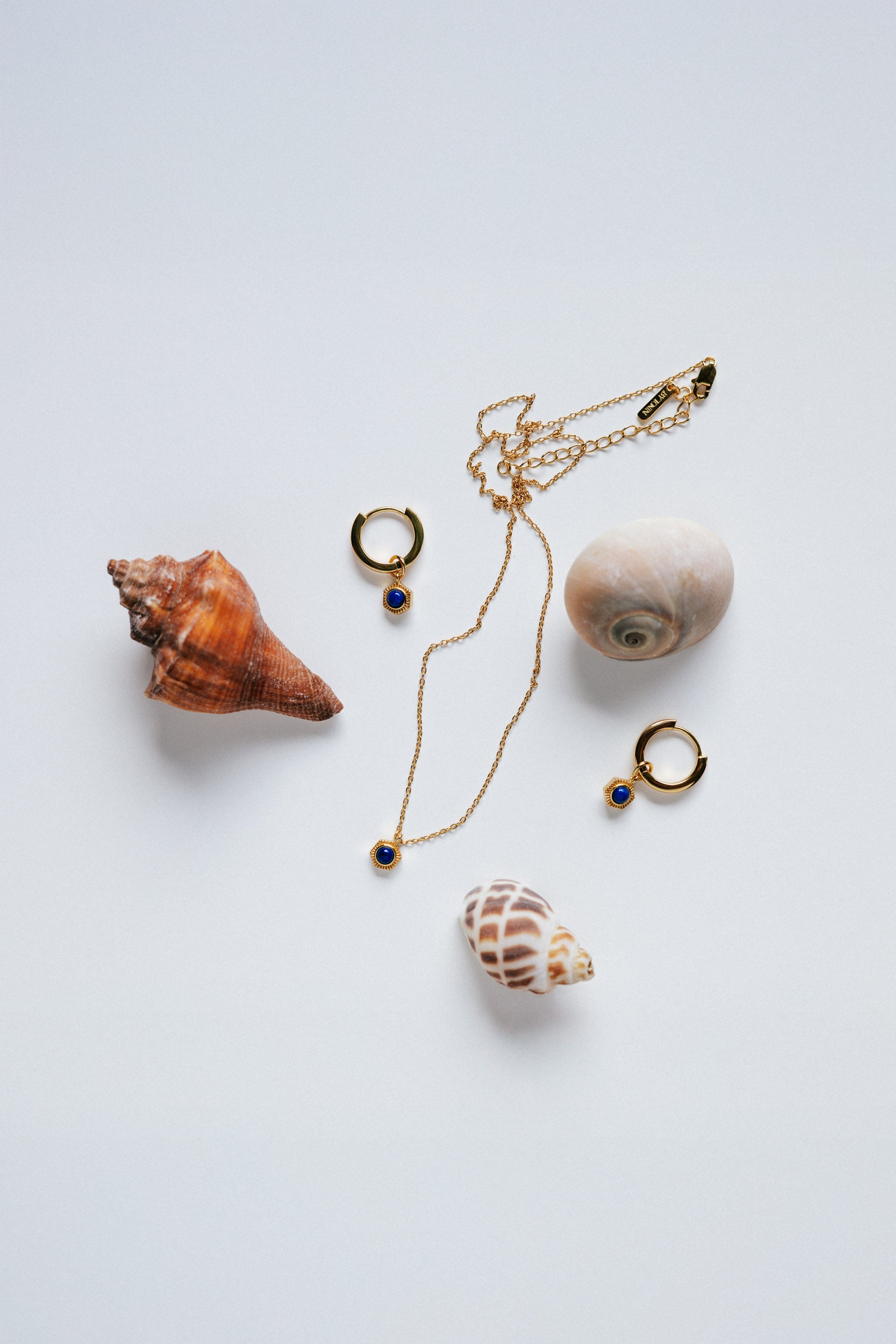 Set - Round Lapis Lazuli pendant necklace and huggie hoop earrings set, styled with mixed natural seashells on a white background