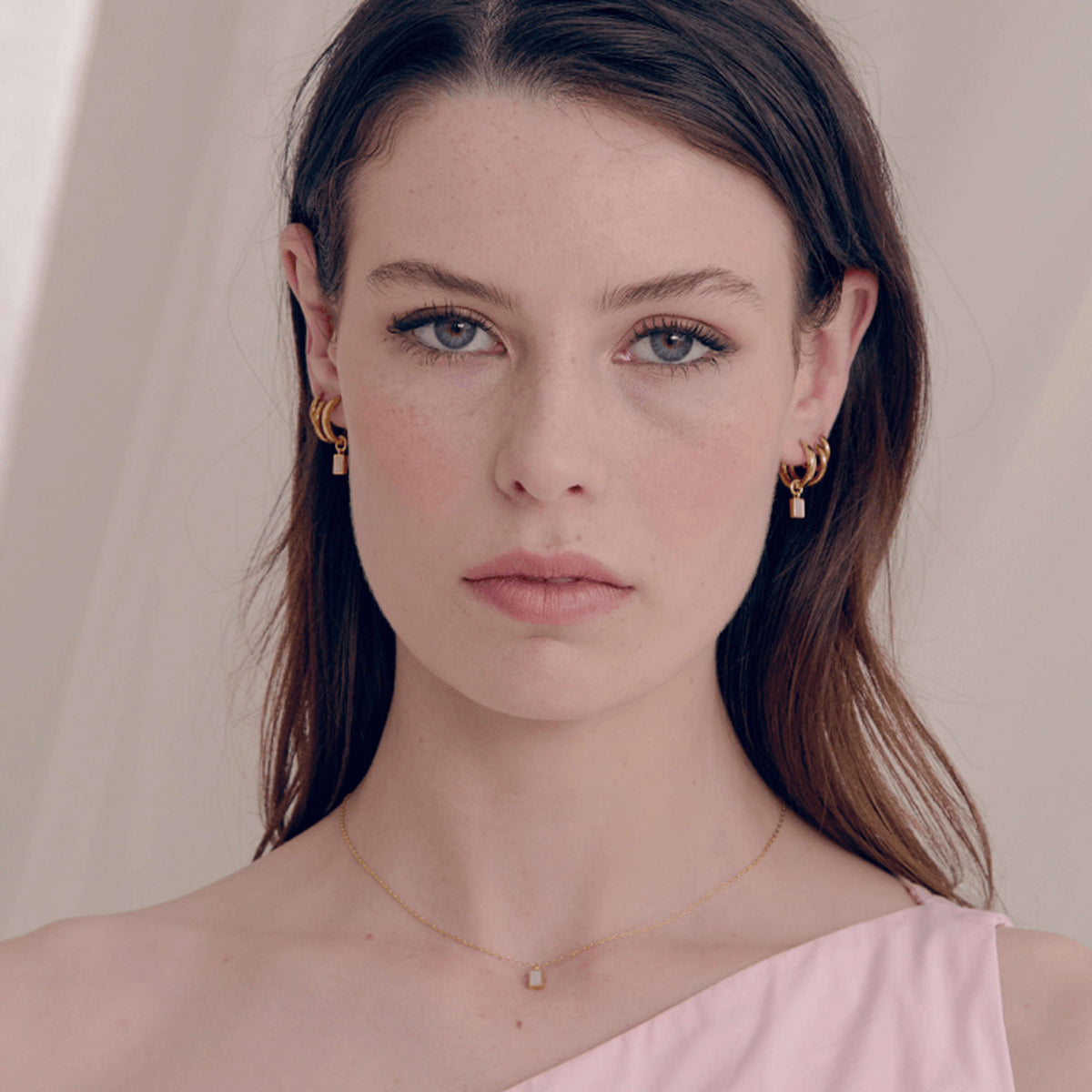 Woman wearing gold earrings and a delicate necklace against a plain background