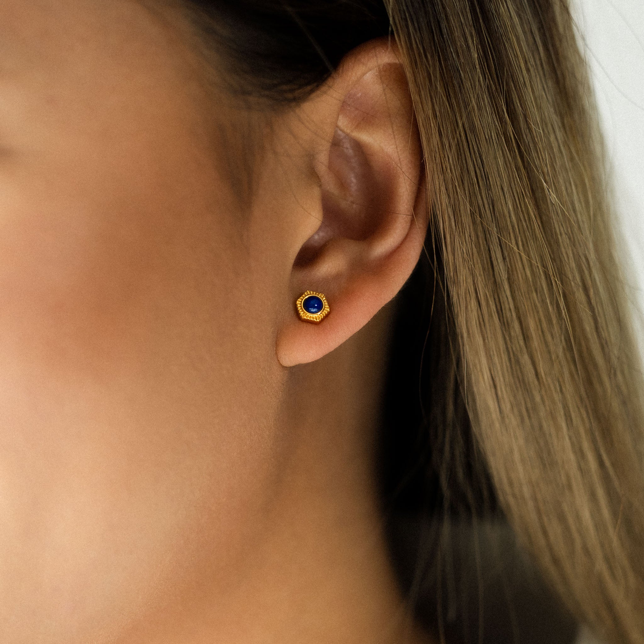 Adorn your ear with BY TONIN's captivating Bel e Viv gold hexagon stud earring, beautifully showcasing a deep blue lapis lazuli gemstone in a striking close-up.