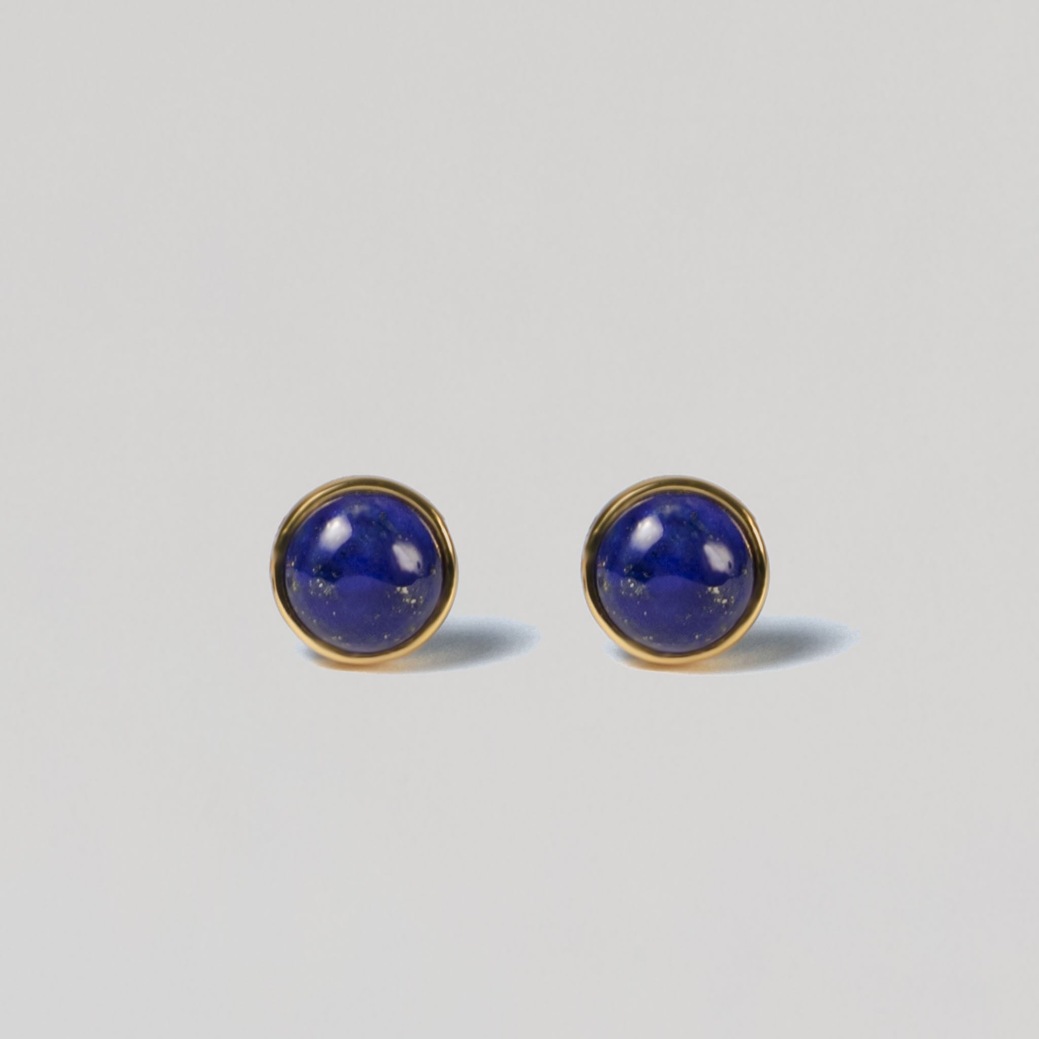 Illuminate your look with BY TONIN's Bel e Viv gold round stud earrings, showcasing captivating deep blue lapis lazuli on a crisp, light grey background for timeless appeal.