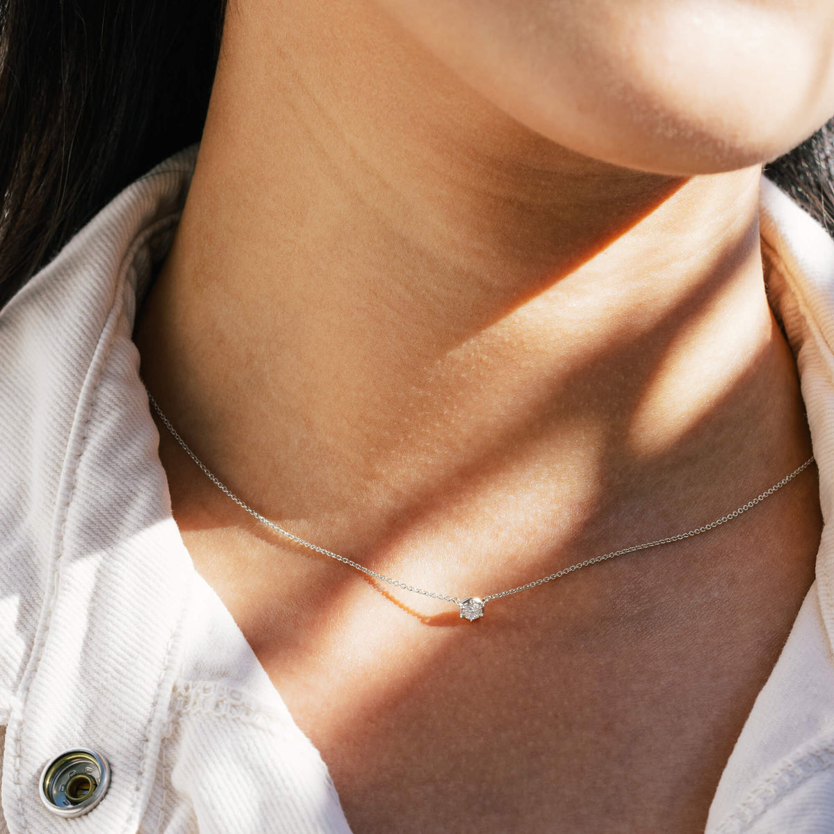 A close-up detail of the 925 sterling silver 0.2 carat lab diamond necklace framed by a white denim shirt collar, demonstrating how the delicate chain functions as a foundational piece for everyday jewellery layering.