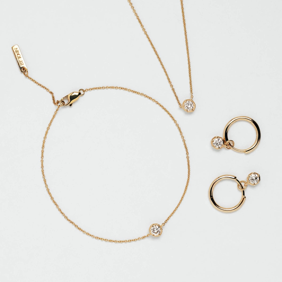 A gold jewellery set in New Zealand featuring a delicate chain necklace, matching bracelet, hoop earrings, and a small ring, each adorned with a clear lab diamond, displayed on a clean white background.
