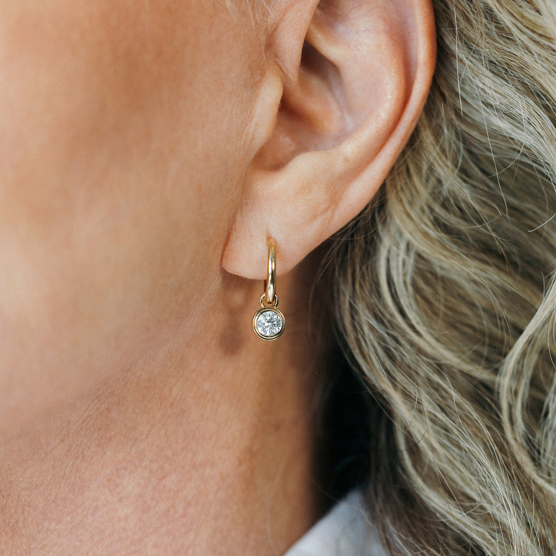 Solid gold solitaire lab grown diamond drop earrings by New Zealand brand BY TONIN, featuring bezel-set round brilliant diamond on ear lobe.