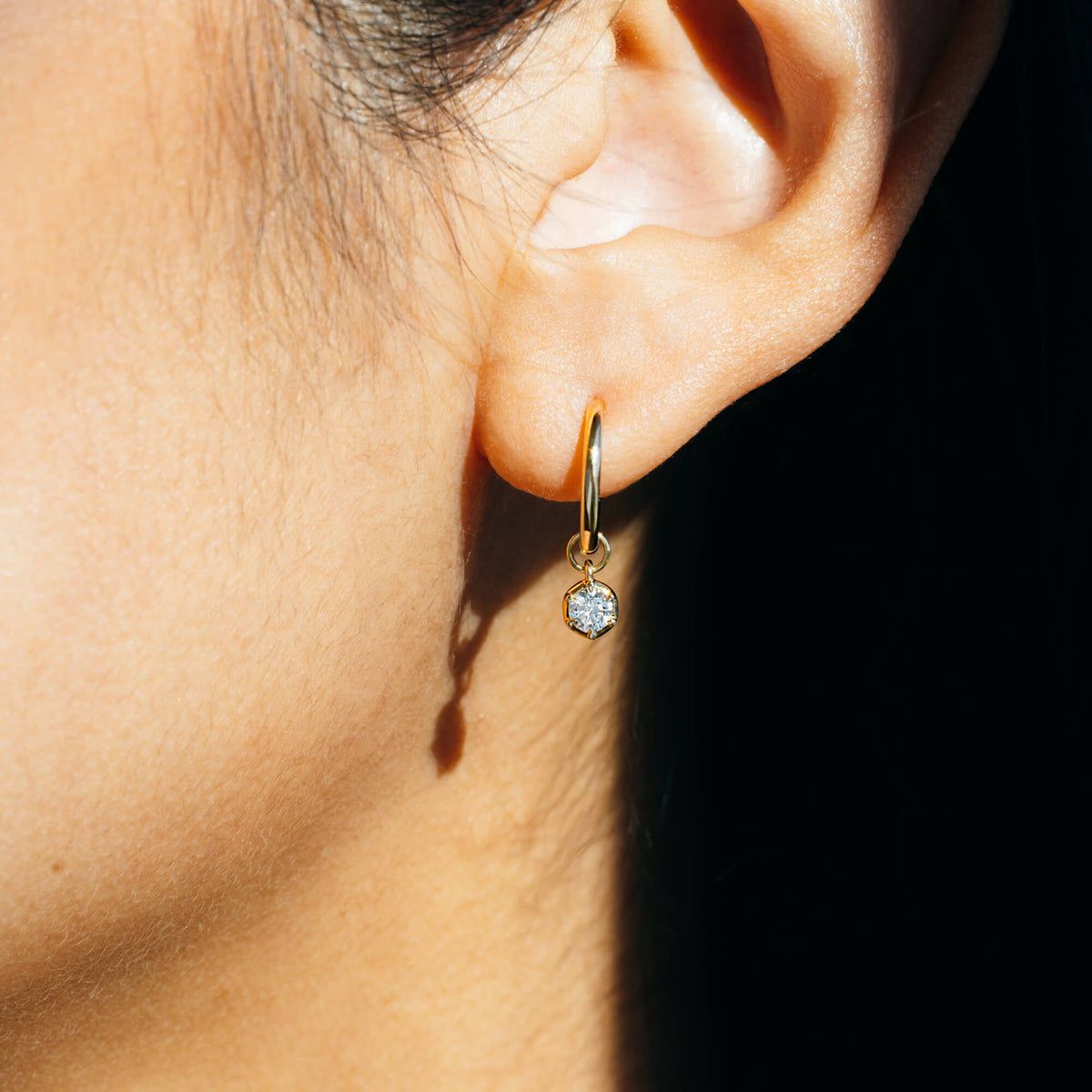 Detailed close-up of a 9K gold small hoop earring featuring a single bezel-set 0.2 ct lab-grown diamond drop charm, demonstrating scale and clarity under natural direct lighting conditions in NZ