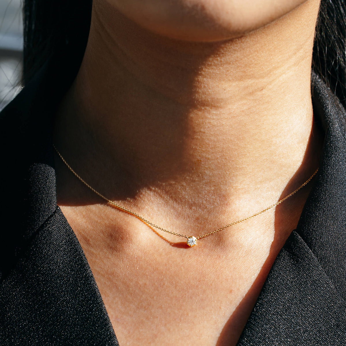 Close-up detail of a model wearing the delicate 9K gold chain necklace from the BY TONIN Essential Diamond Collection, showcasing the scale of the brilliant-cut solitary diamond charm sitting gently on the collarbone.